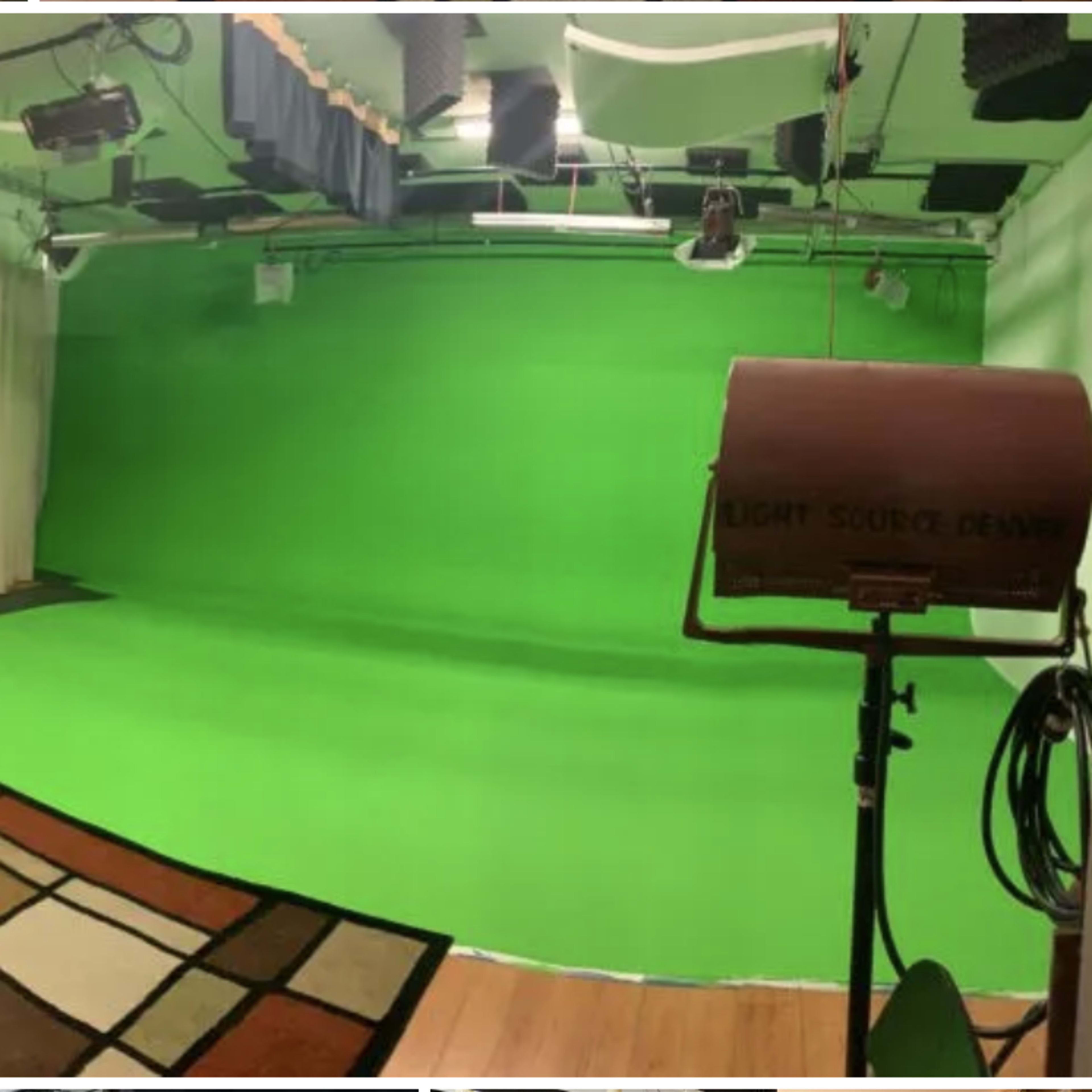 A green screen studio with a wooden floor, a patterned rug, and studio lighting equipment.