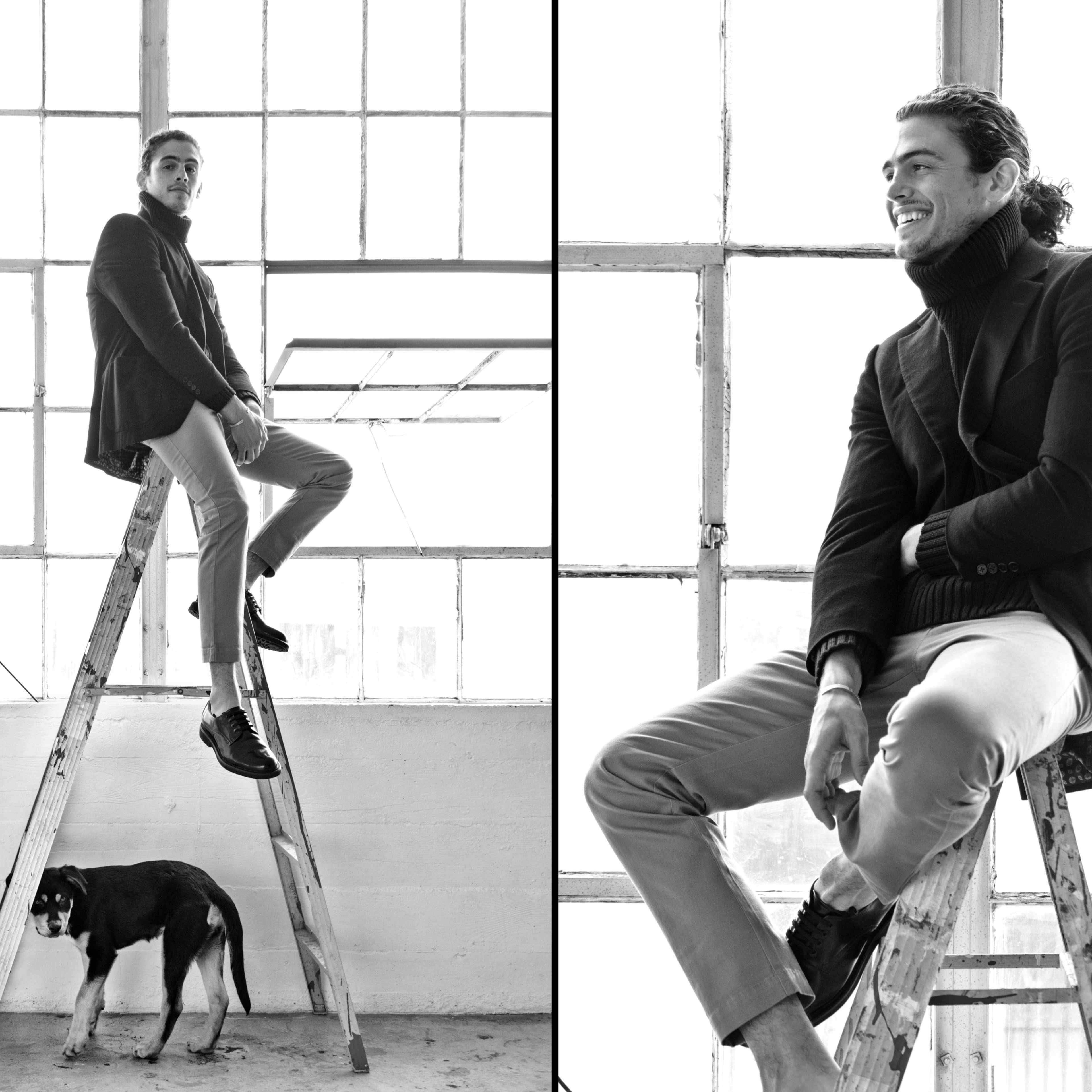 A man sits on a ladder inside a bright, industrial space while a dog stands beside him on the floor.