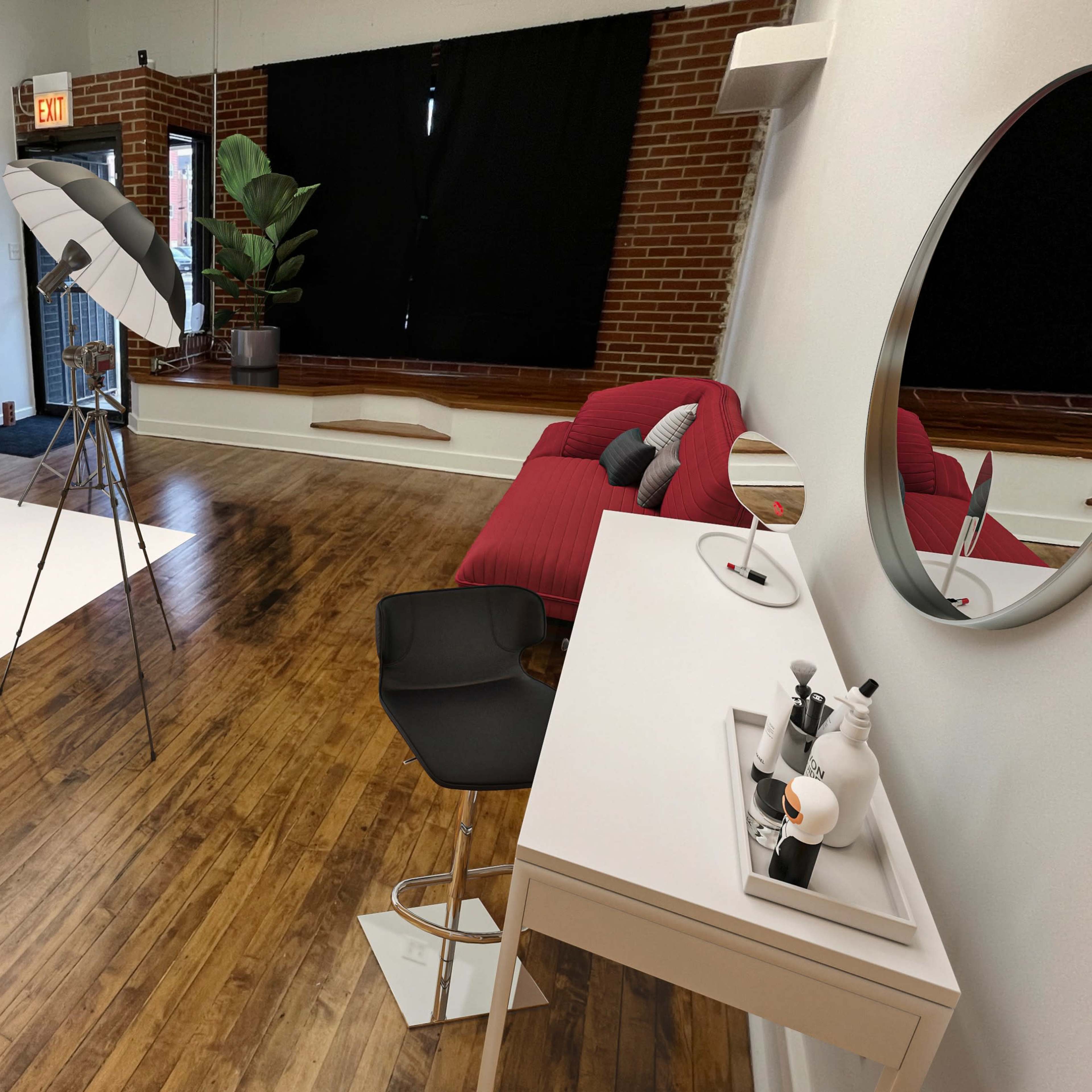 A photography studio with a white backdrop, two lighting setups, a red couch, and a vanity table with makeup items.