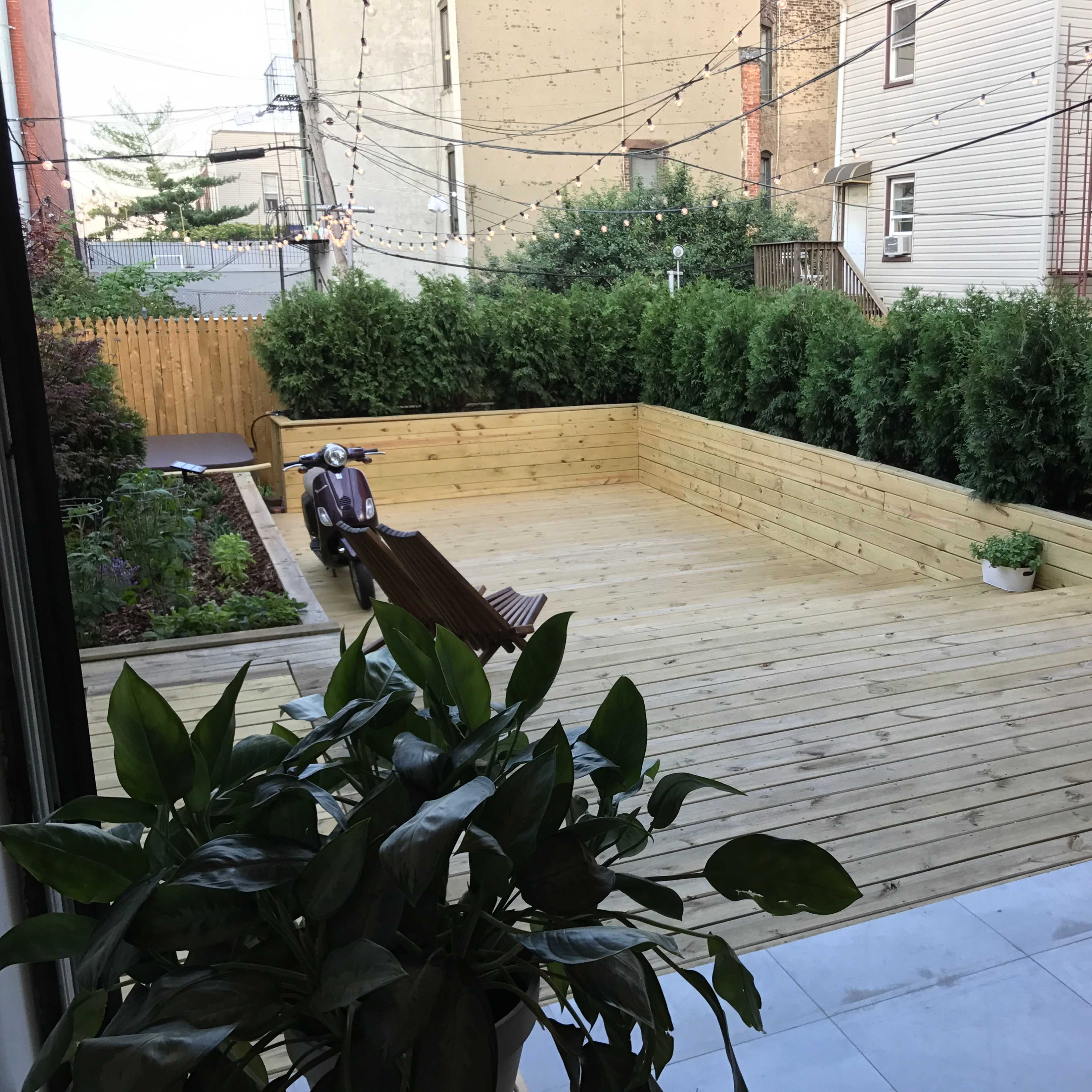 A wooden deck surrounded by greenery, with a vintage scooter and a bicycle parked nearby.
