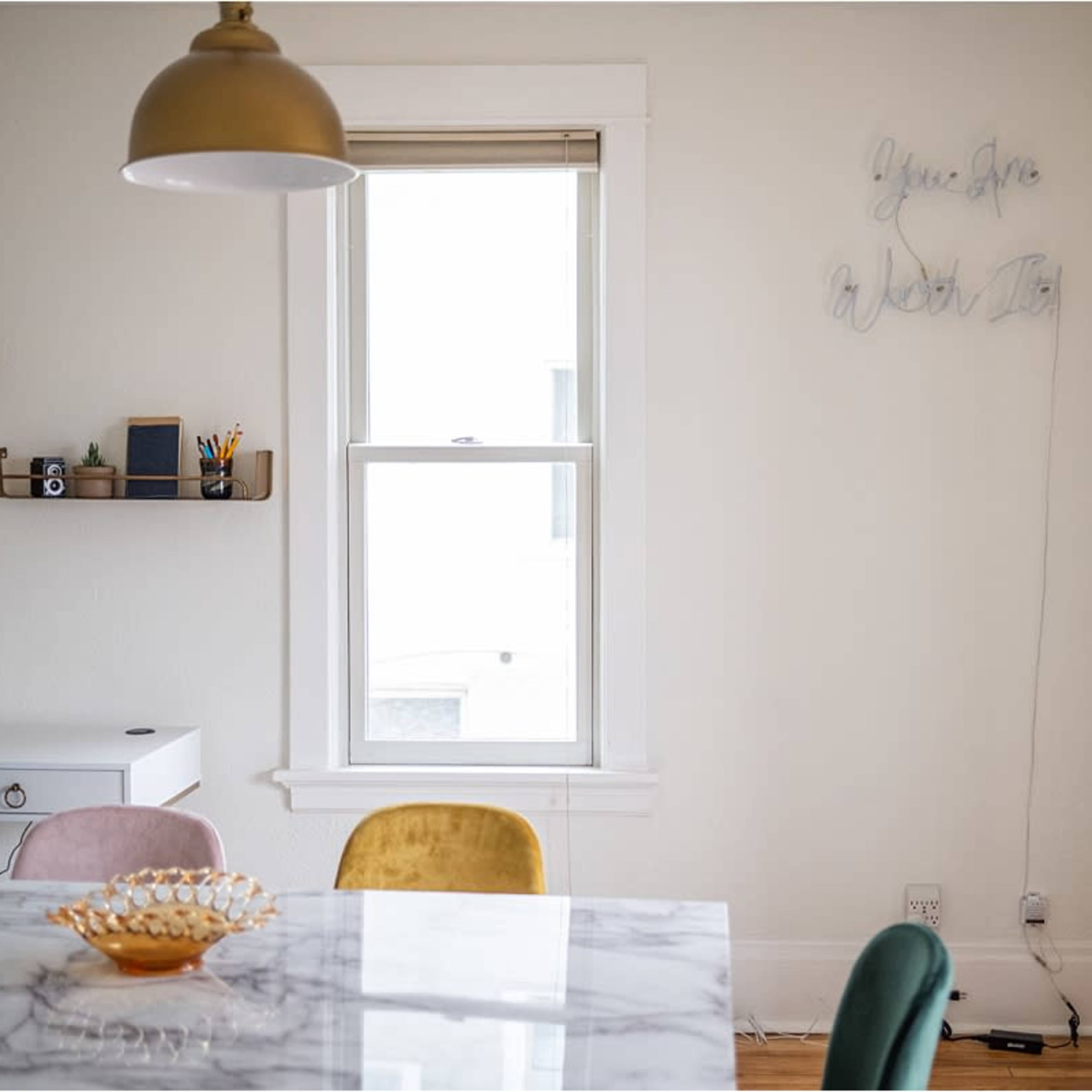 A dining area features a marble table, colorful chairs, and a wall with decorative lighting that spells out a motivational phrase.