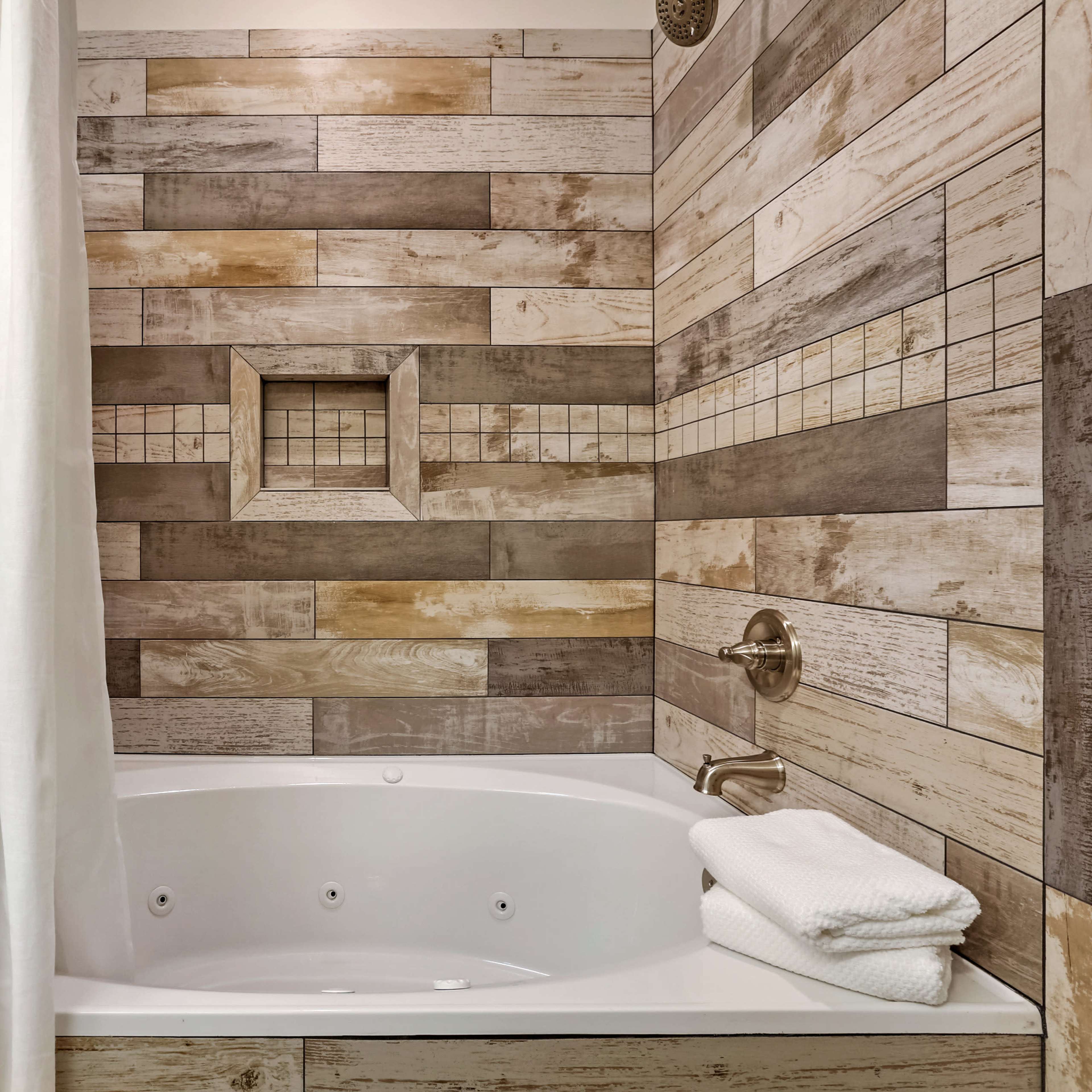 A bathroom with a white bathtub surrounded by wooden wall panels and a striped shower curtain.