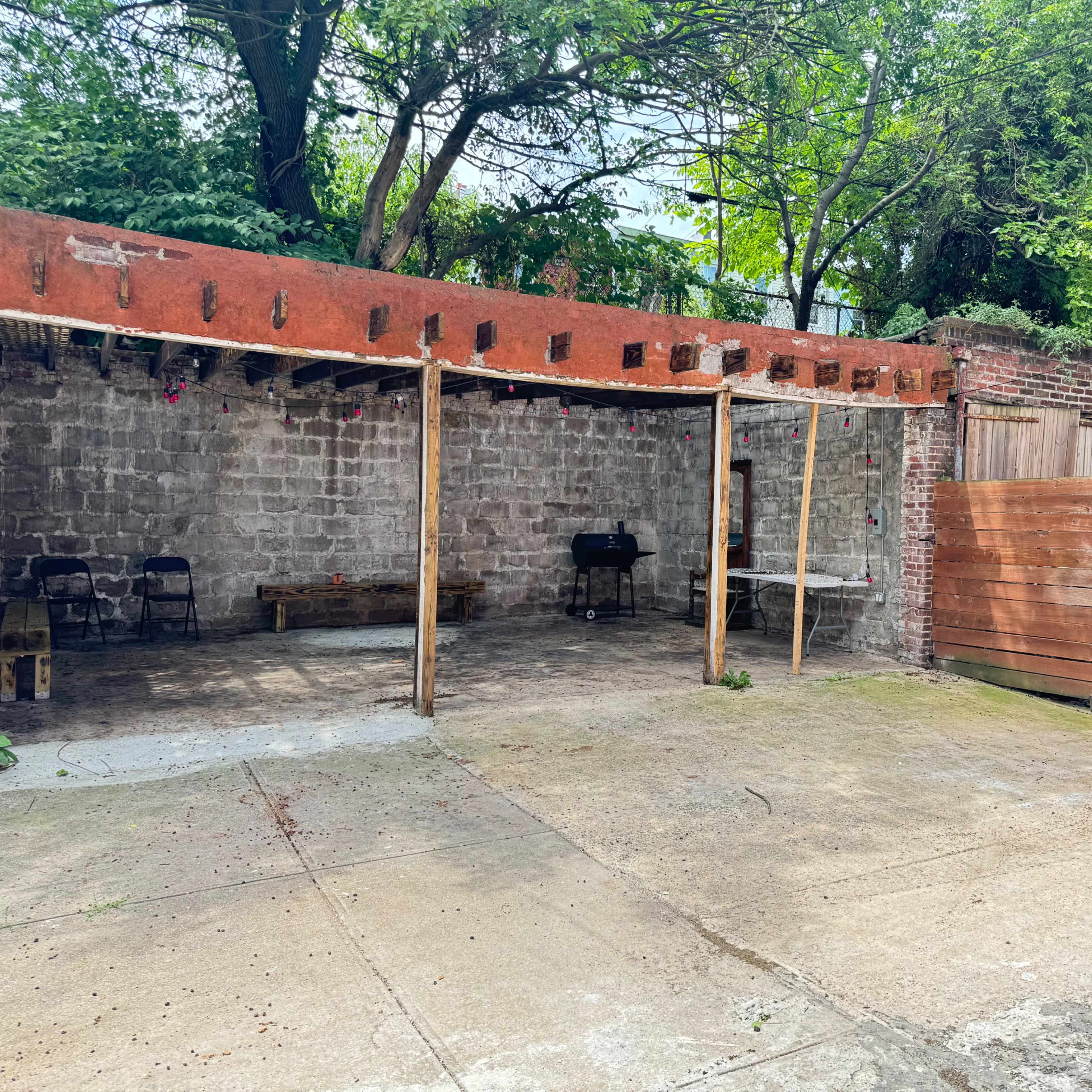 A partially open outdoor space with a concrete floor, a stone wall in the background, and wooden fencing on one side.