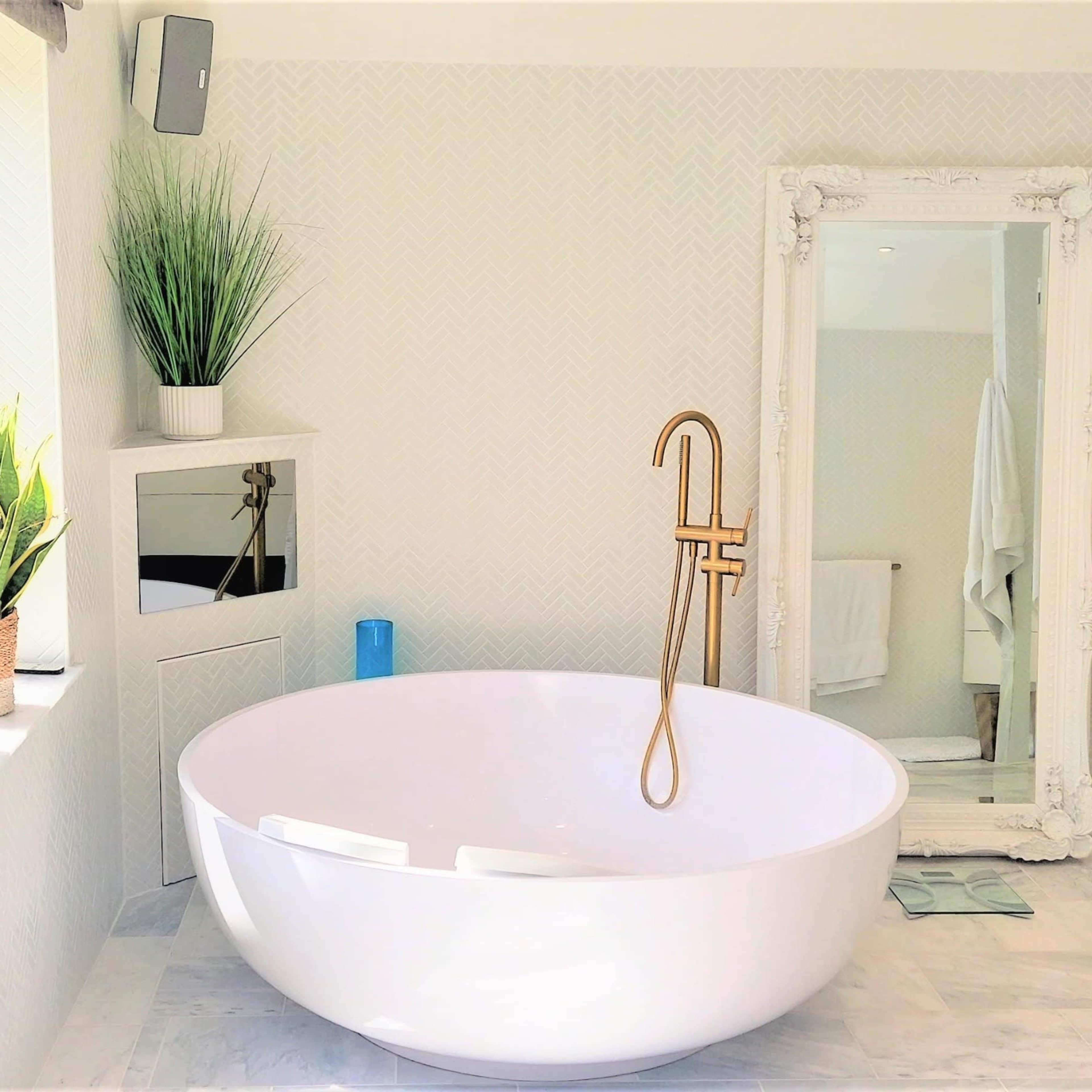 A modern bathroom featuring a freestanding white bathtub, a large mirror, potted plants, and a sleek vanity.