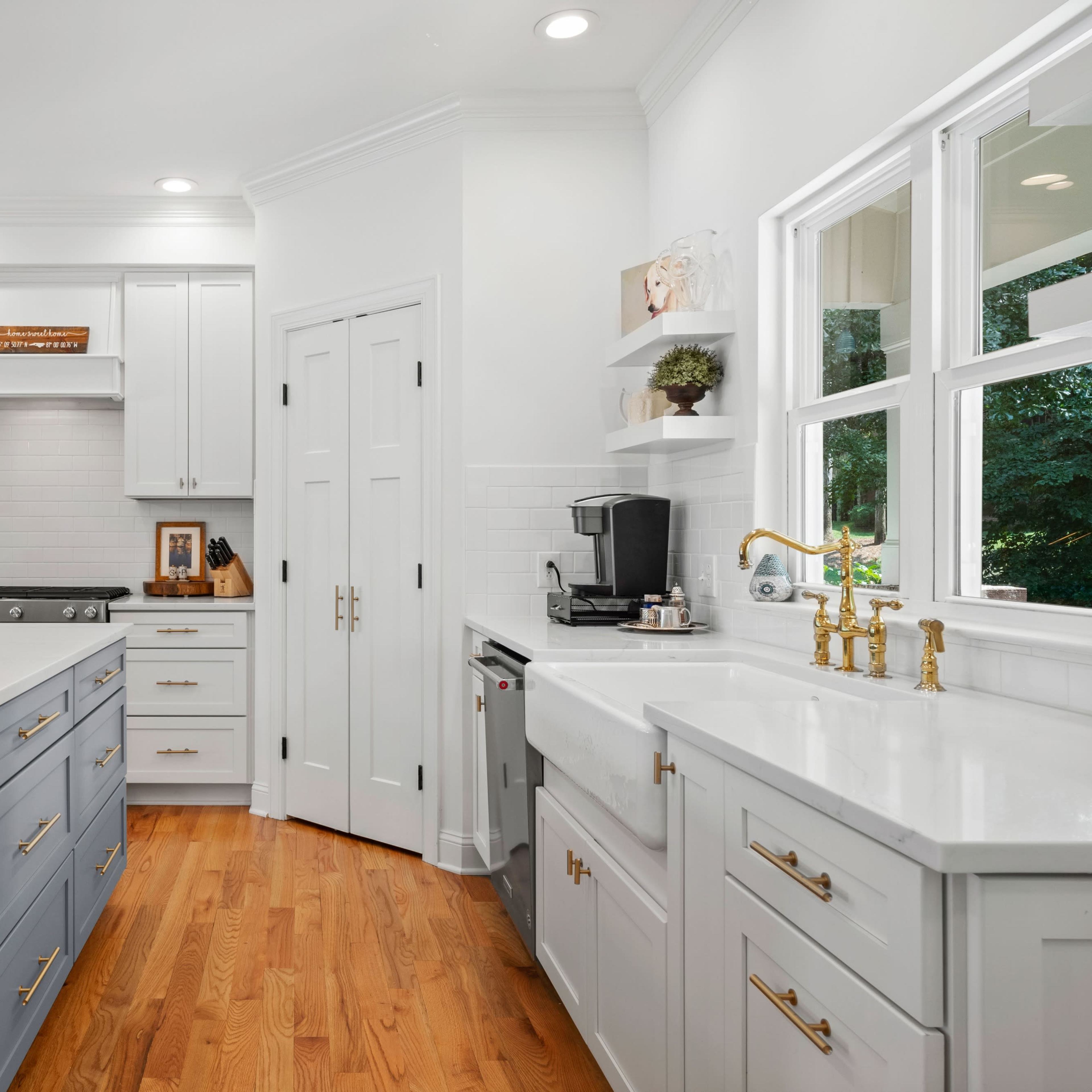 The kitchen features a spacious layout with white cabinetry, a large island, and wooden flooring.