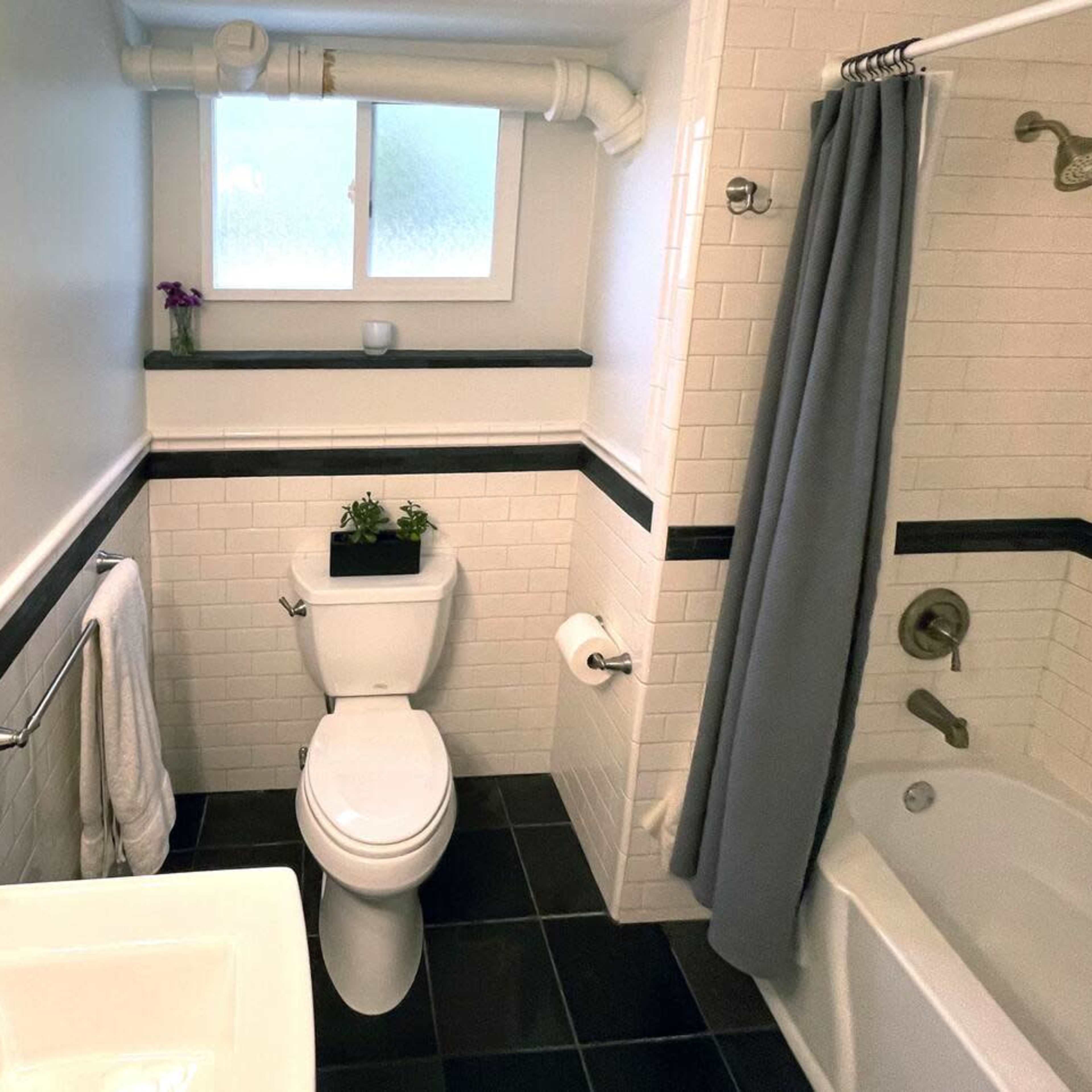 A small bathroom featuring a toilet, sink, bathtub, and a window, with black and white tiled walls and a gray shower curtain.