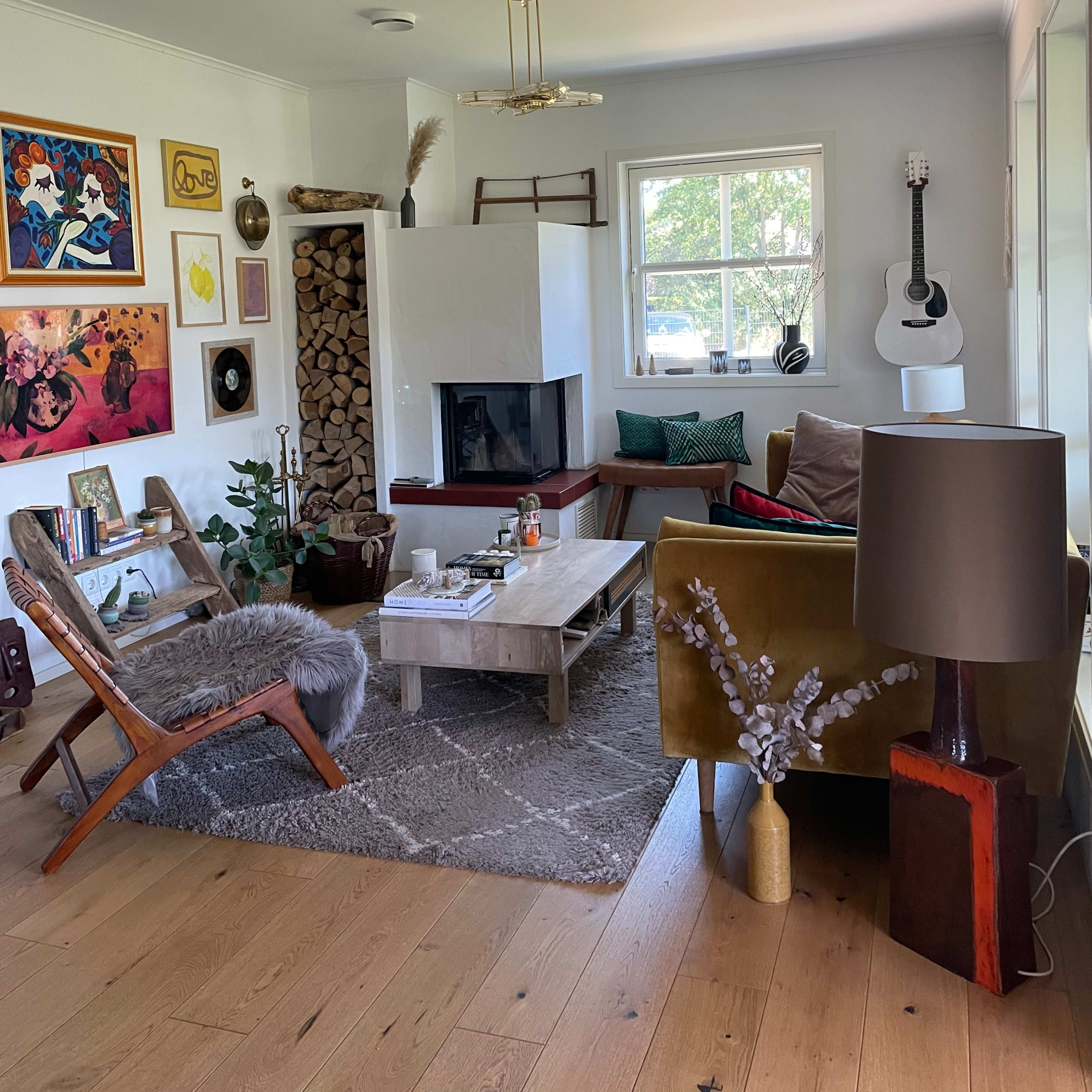 A cozy living room featuring a fireplace, a wooden coffee table, eclectic artwork on the walls, and a guitar in the corner.
