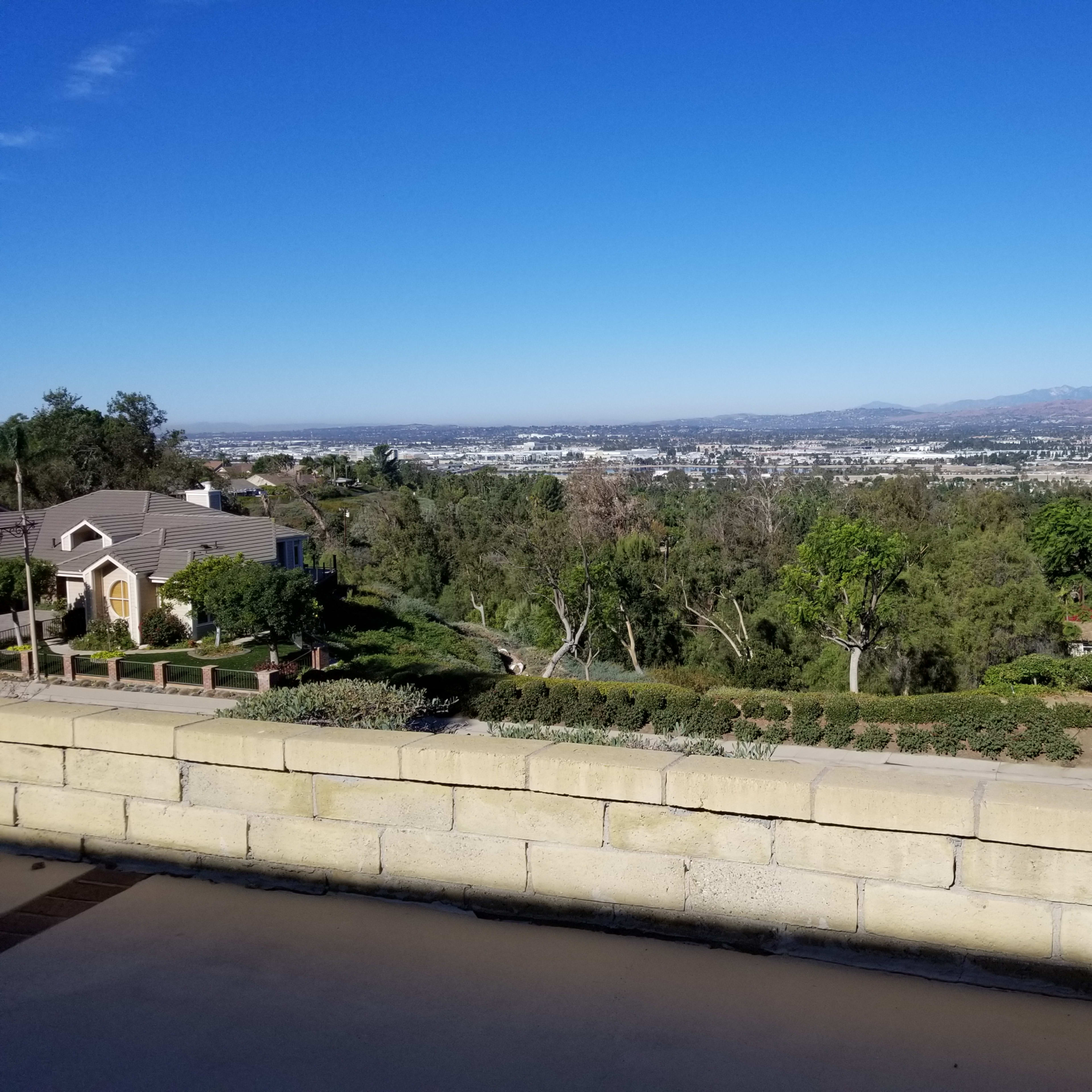 A view overlooking a cityscape surrounded by trees and hills under a clear blue sky.