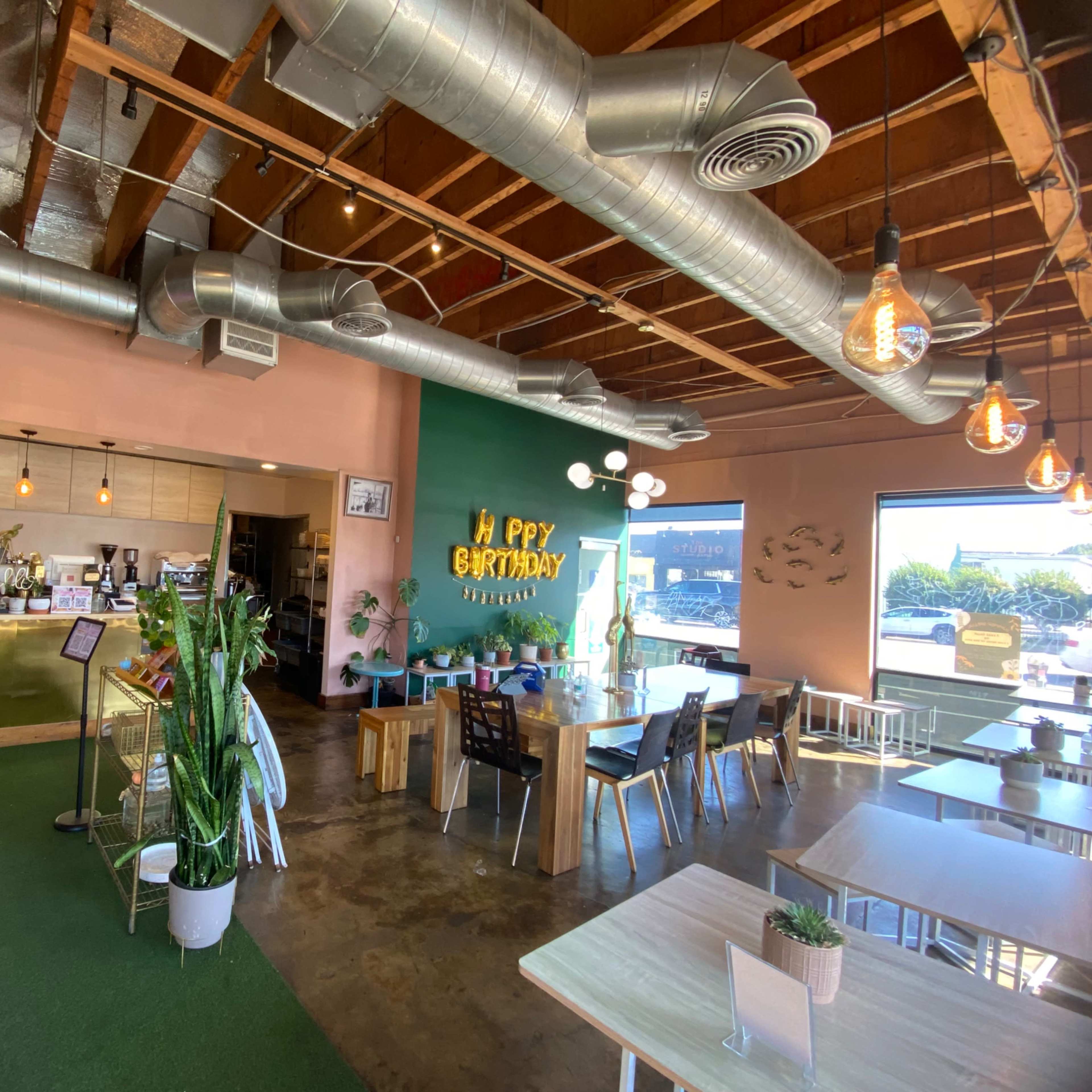 A bright and modern café interior with a green accent wall, birthday decorations, and both seating and a service counter.