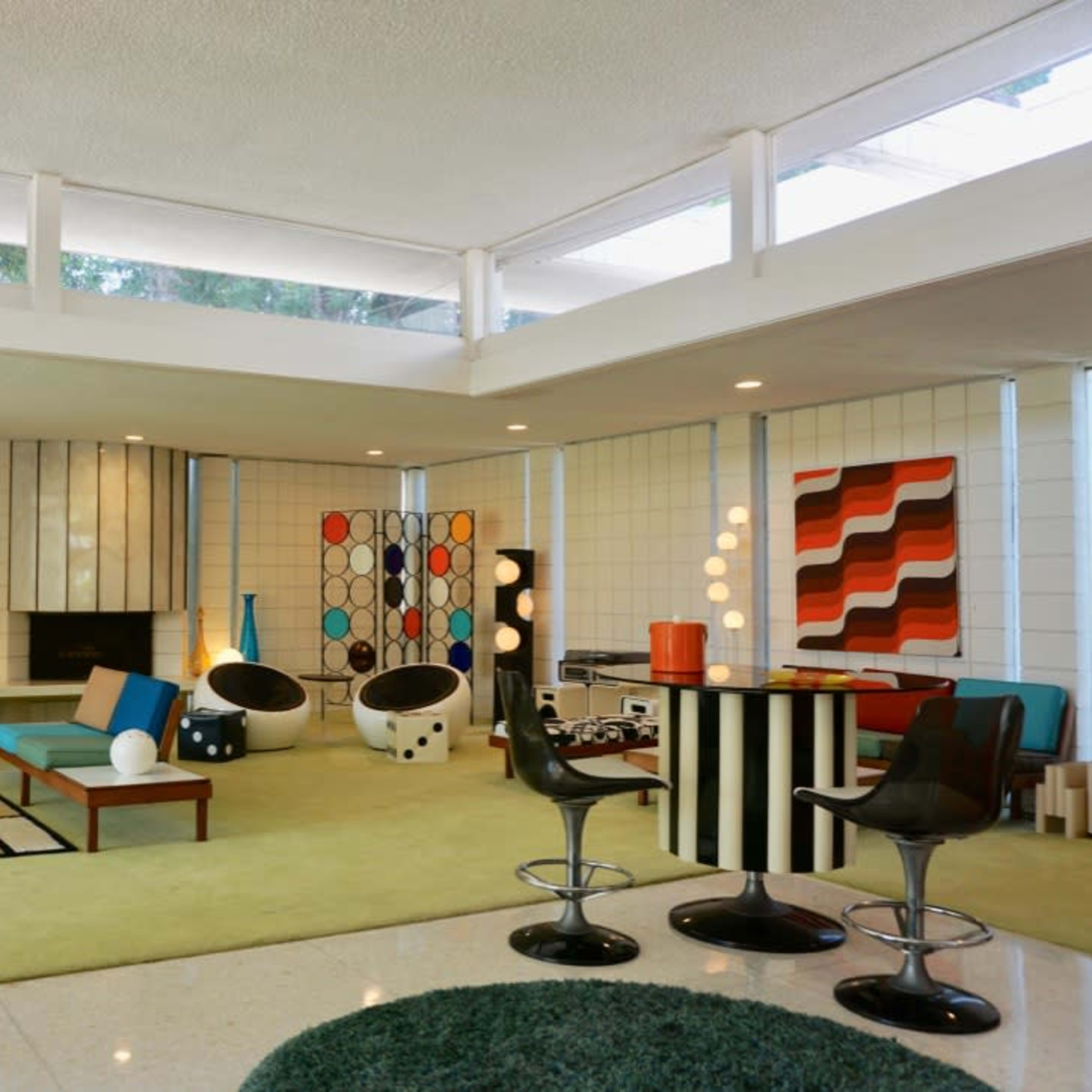 A mid-century modern living room featuring colorful furniture, geometric wall art, and large windows that bring in natural light.