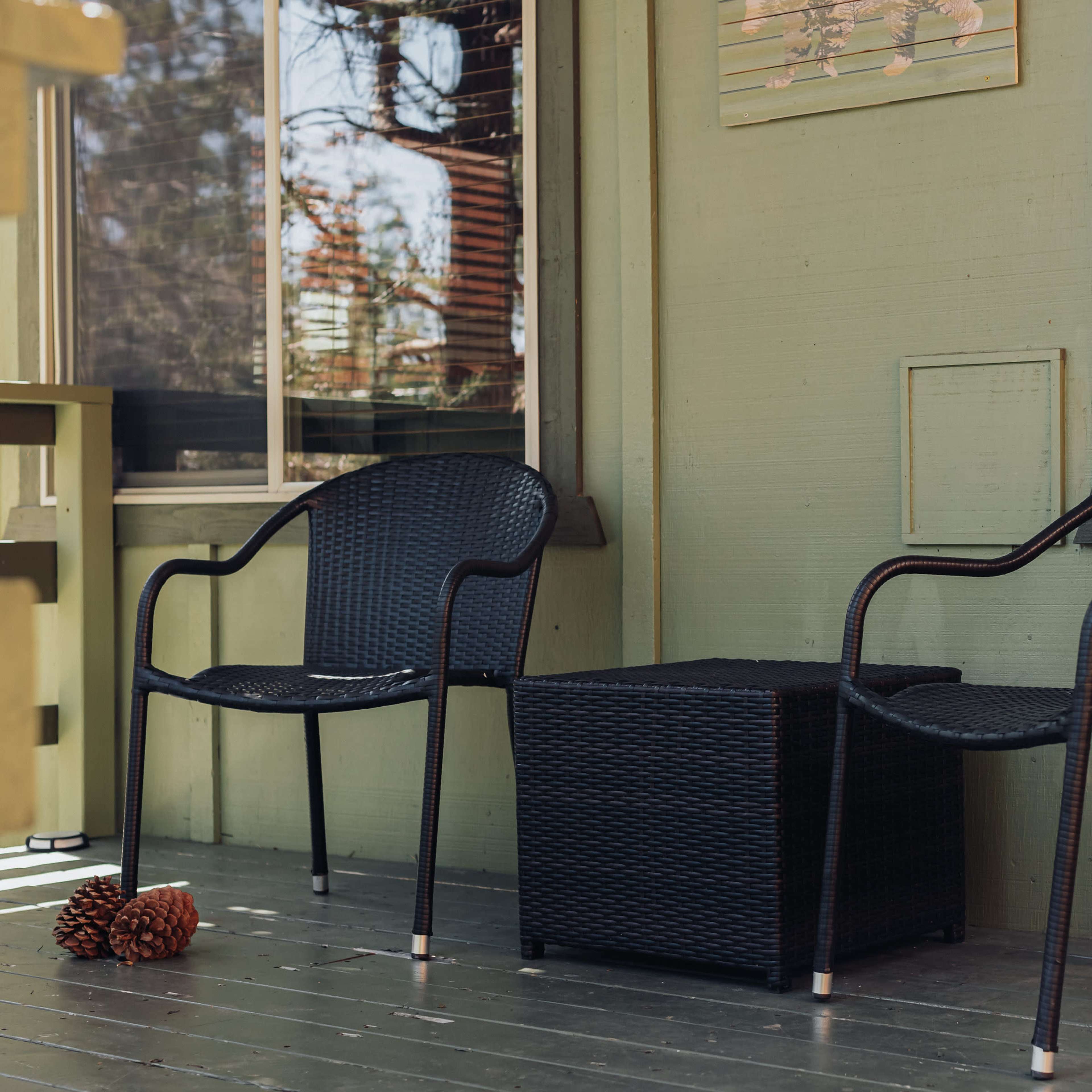 Two black chairs and a small table are positioned on a wooden porch, with a pine cone nearby.