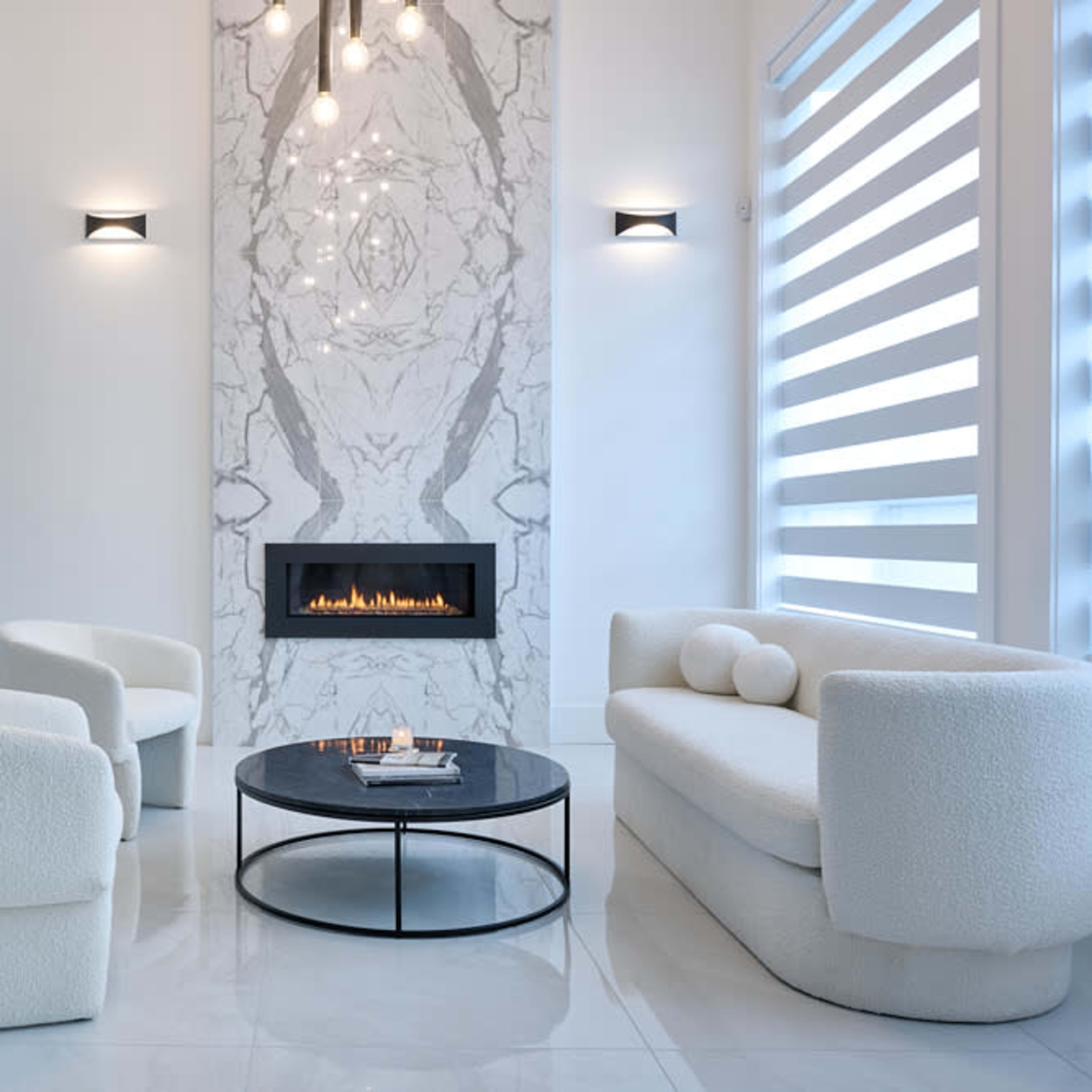 A modern living room features a marble accent wall with a fireplace, two upholstered chairs, a plush sofa, and a round coffee table.