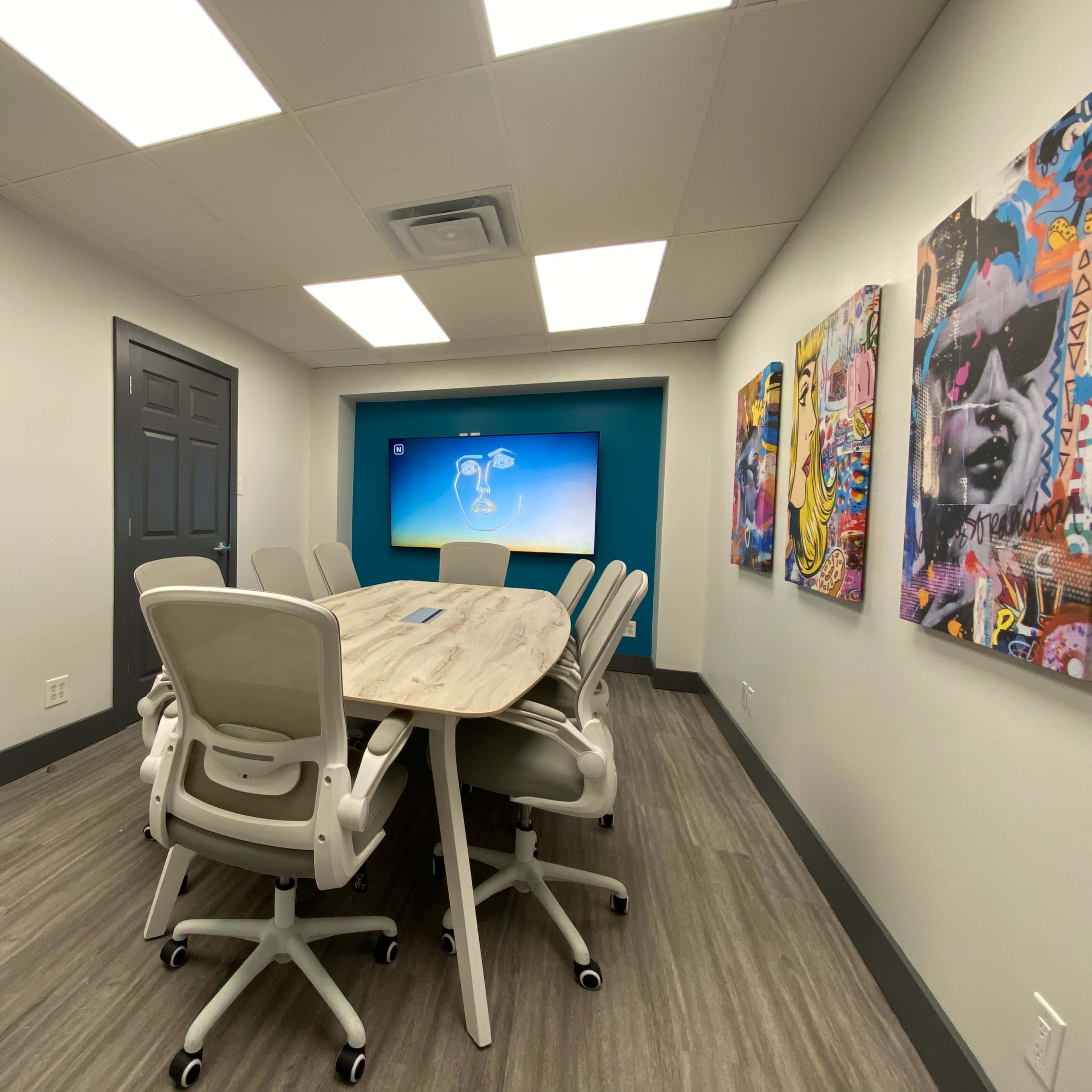 A modern conference room with a large table surrounded by white chairs and a wall-mounted screen displaying a colorful presentation.