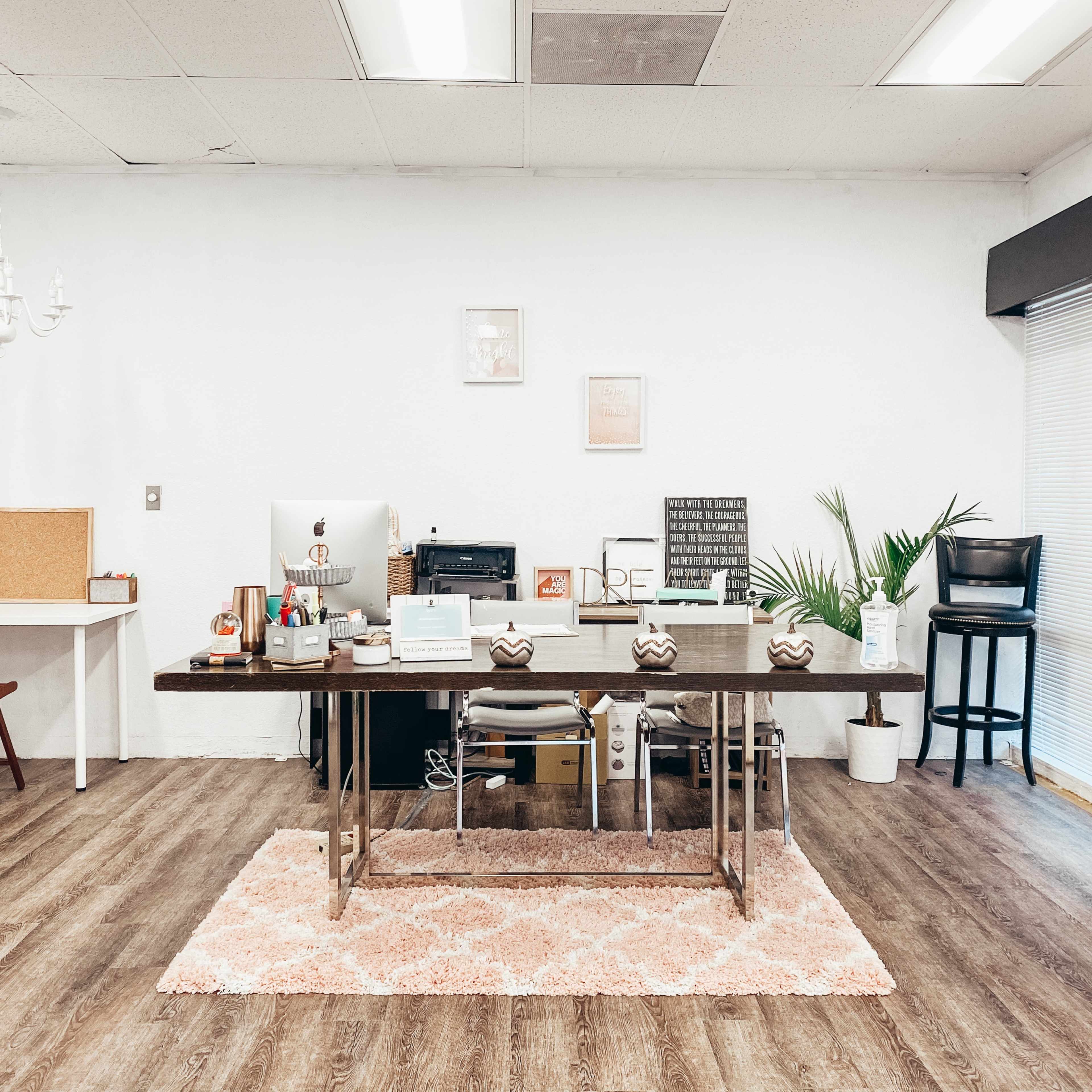 A modern office space featuring a large desk, computer, and various decorative elements against a simple white background.