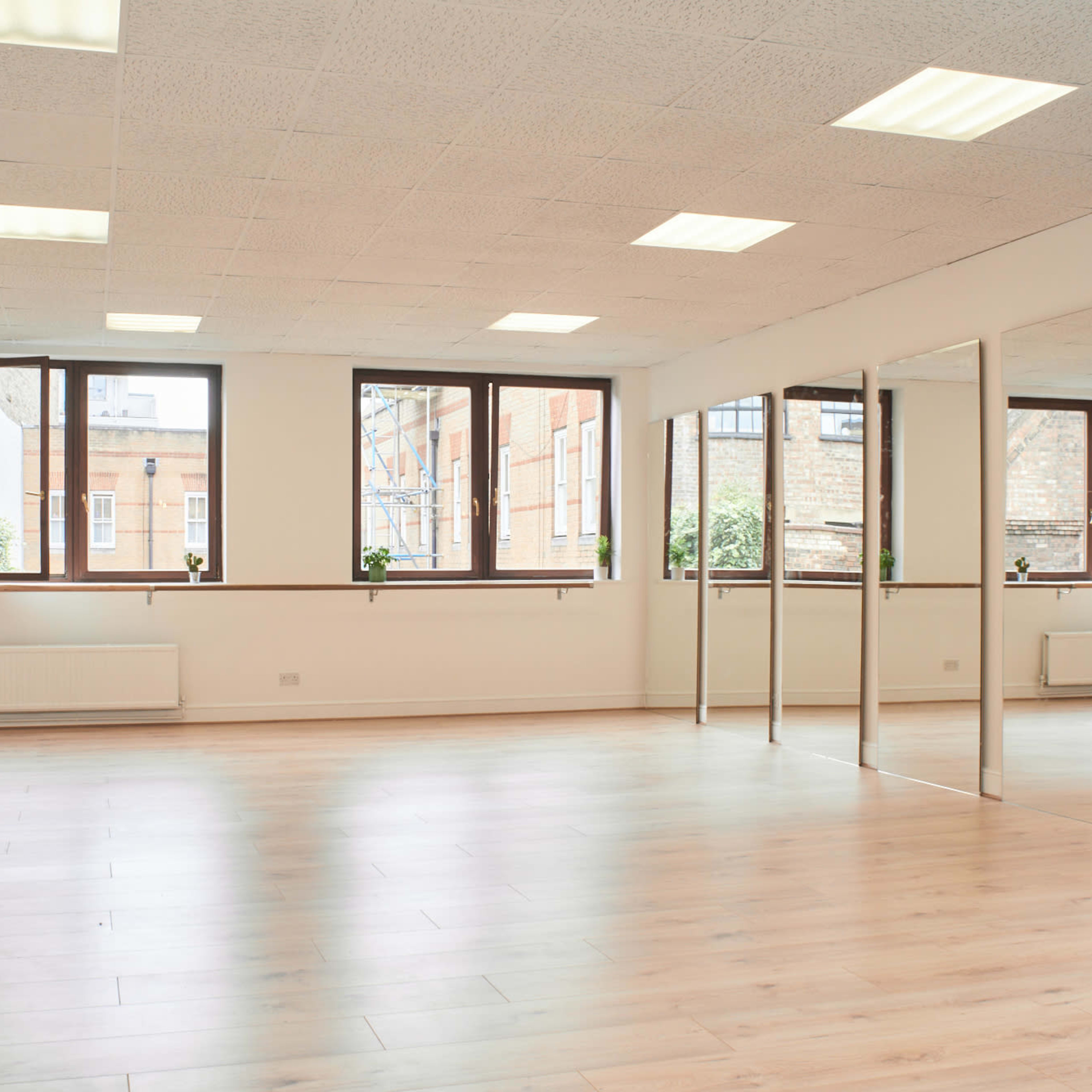 A spacious, well-lit room with large windows, hardwood flooring, and a wall of mirrors.