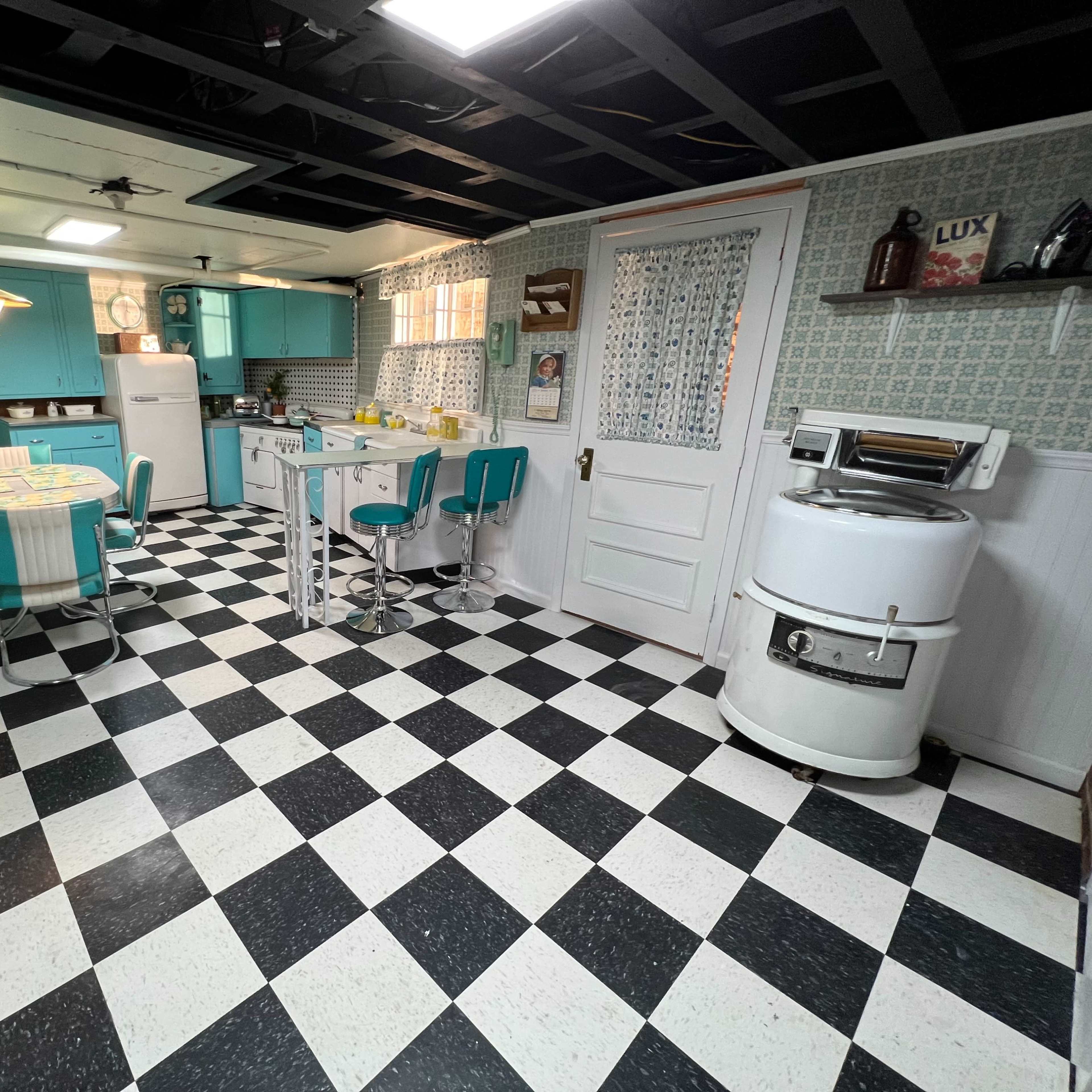 A retro-style kitchen with turquoise cabinets, a checkered black and white floor, a round dining table, and a vintage white stove.