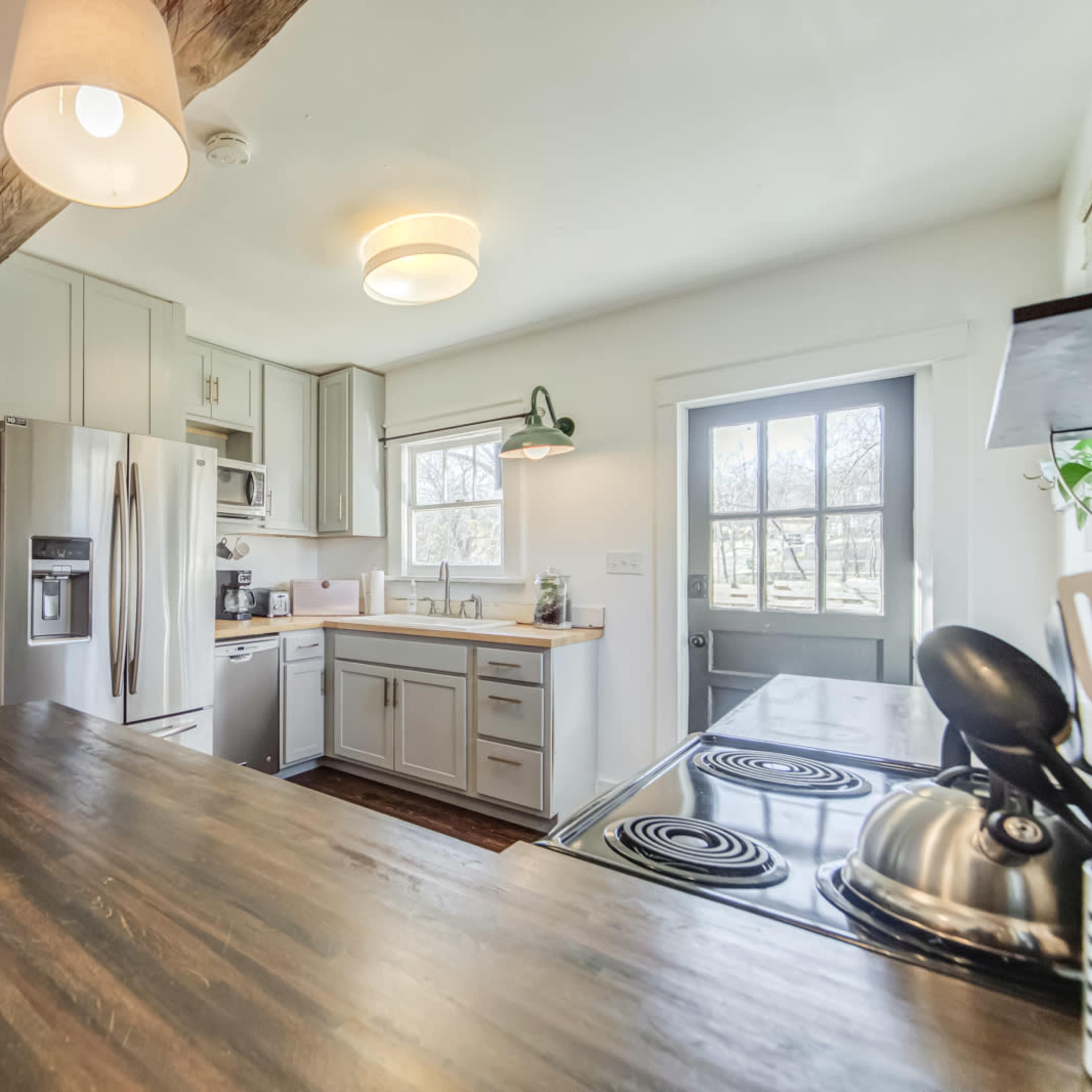 A modern kitchen with light-colored cabinetry, stainless steel appliances, and a wooden countertop, adjacent to a doorway leading to another room.