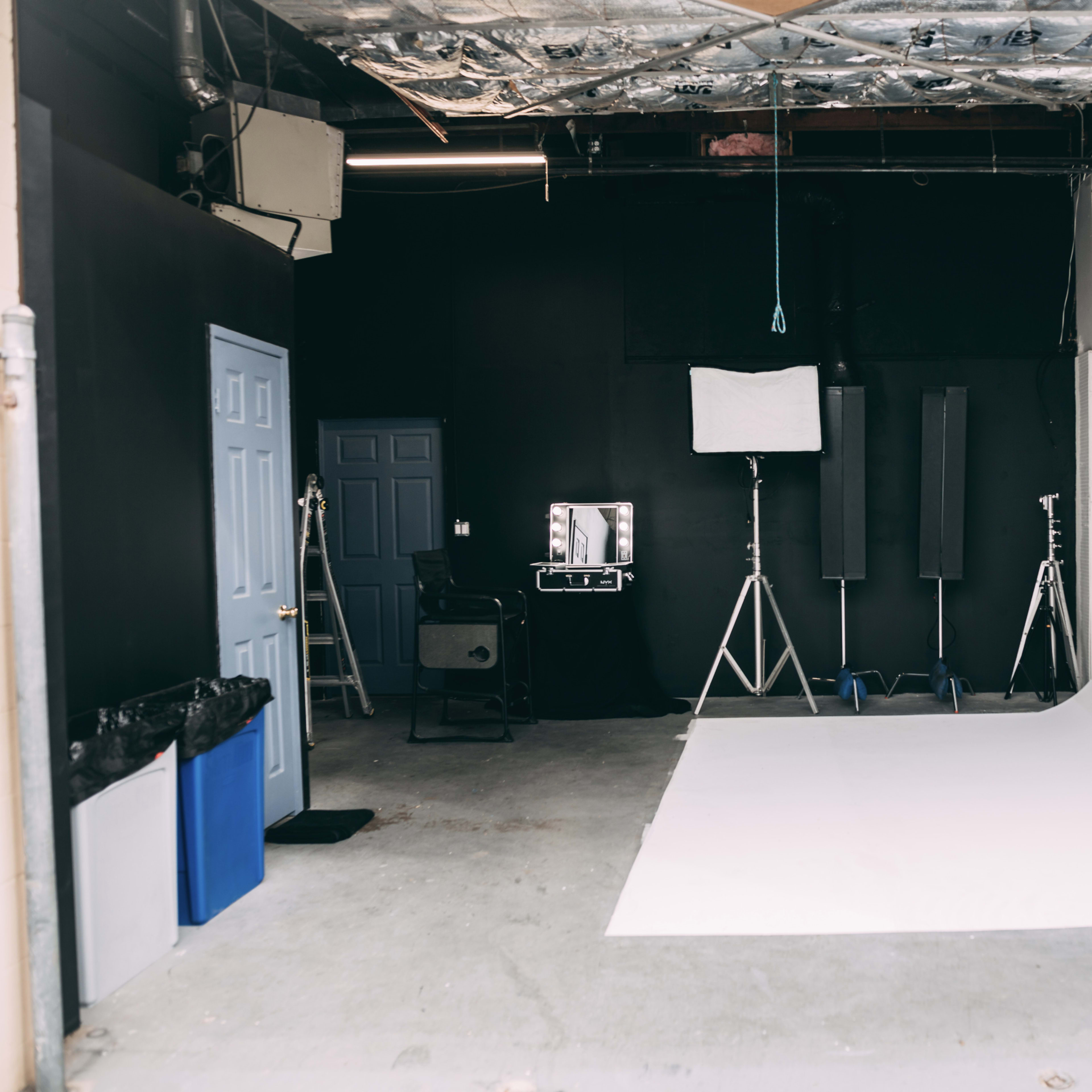 A photography studio with a white backdrop, lighting equipment, and various props arranged in a corner.