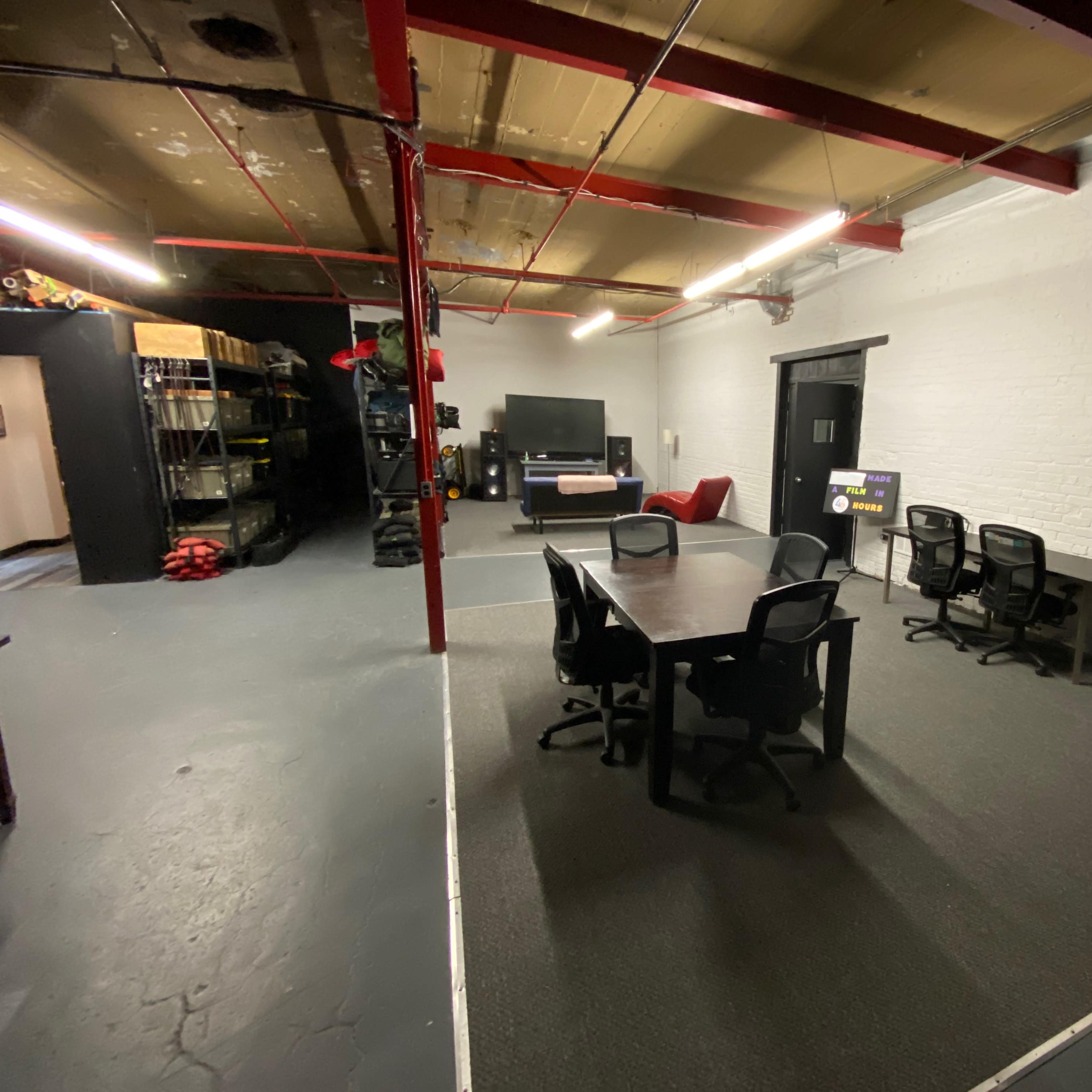 An industrial-style meeting room with a large table and several black chairs, set against a backdrop of white brick walls and exposed red beams.