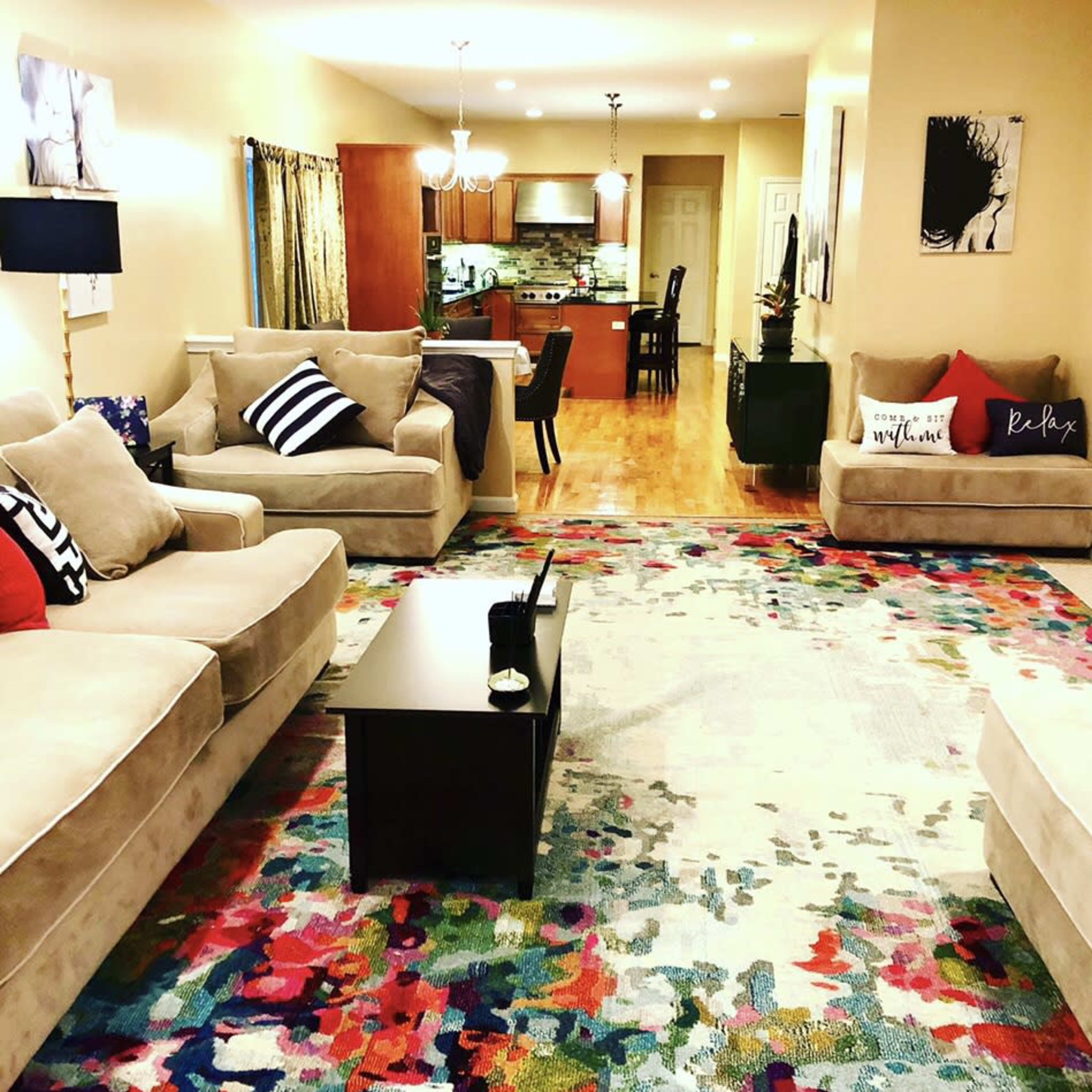 A living room with two beige sofas, a colorful area rug, and a dining area visible in the background.