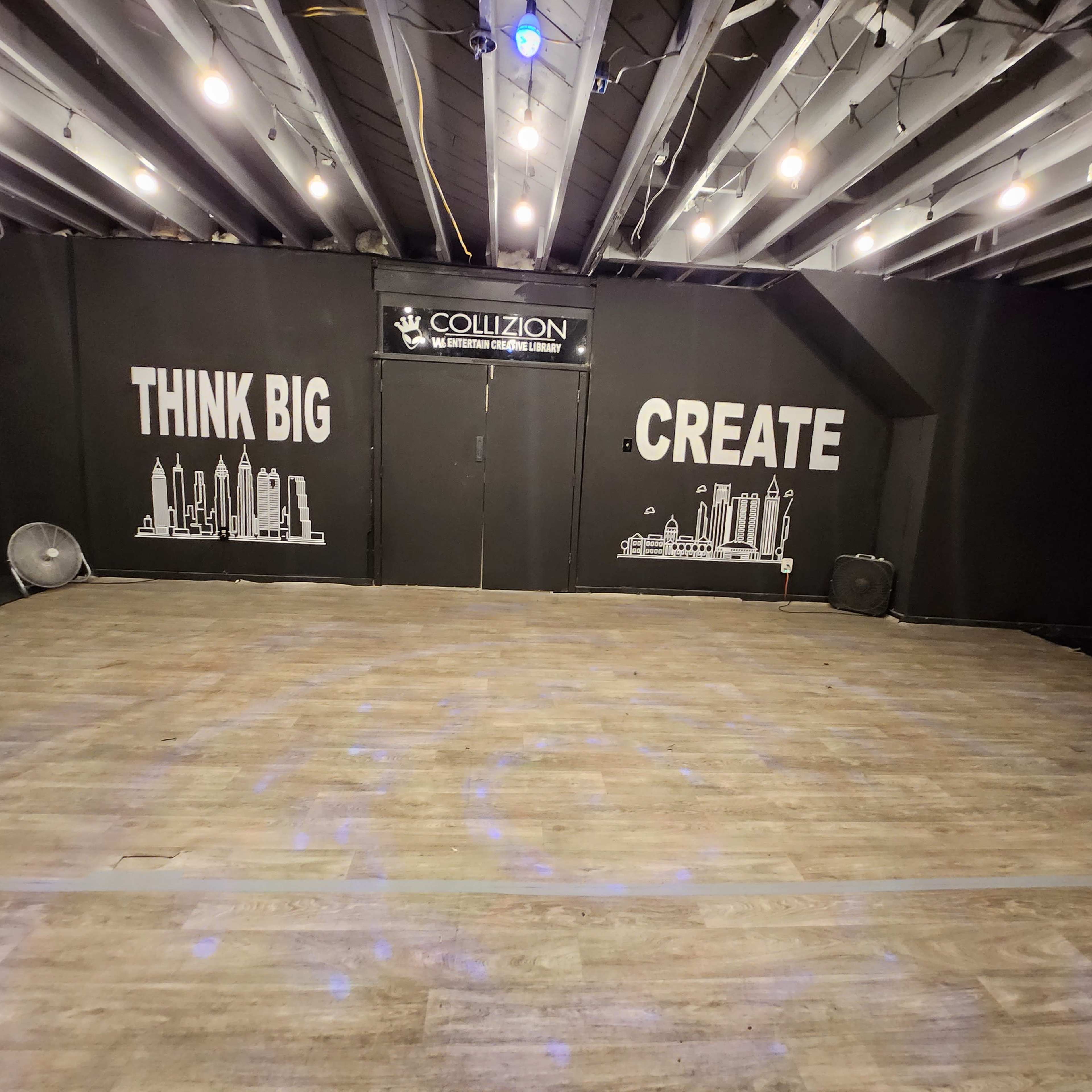 A spacious indoor area with a wooden floor and a black wall featuring the phrases "THINK BIG" and "CREATE" alongside city skyline graphics.