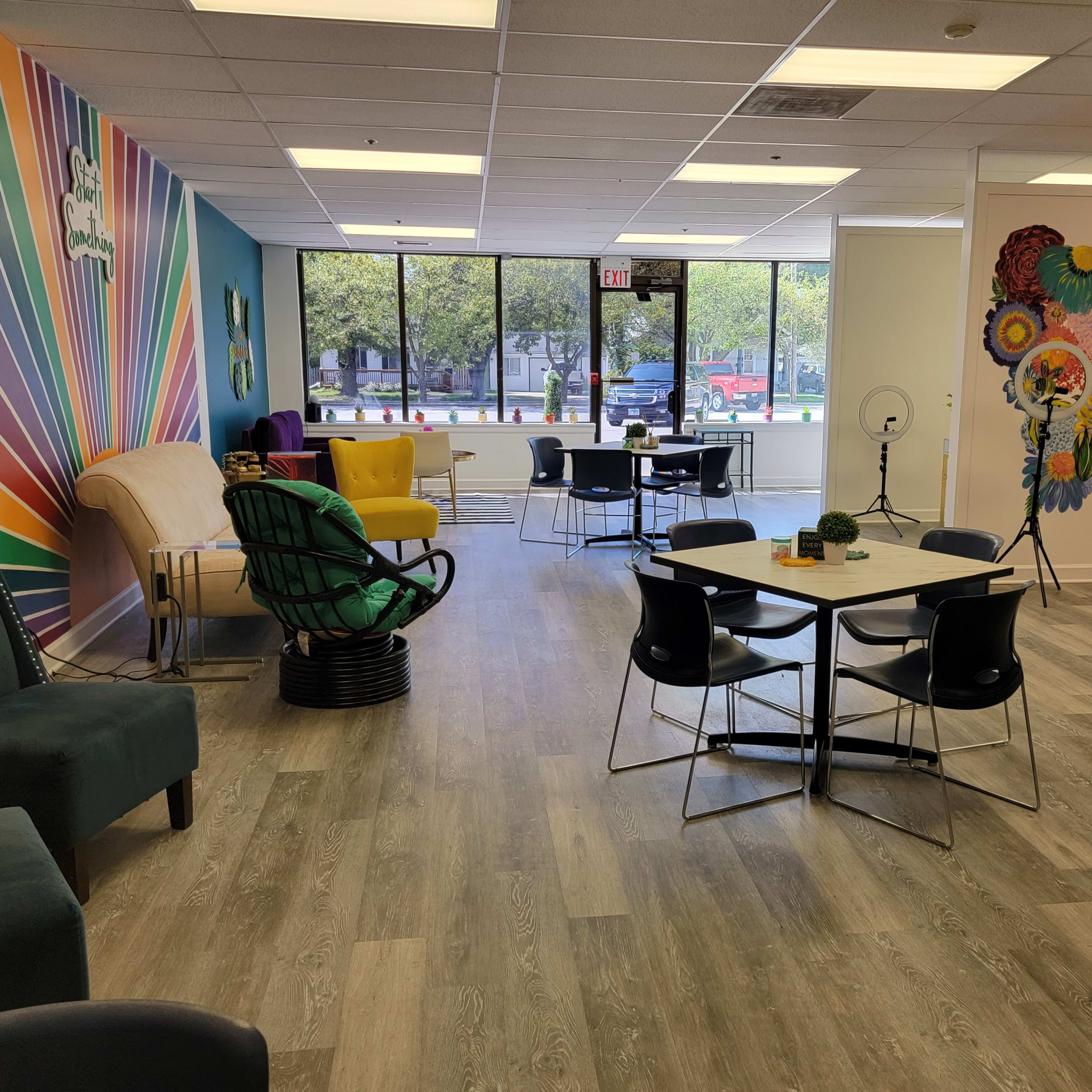 A brightly colored co-working space with modern furniture, including chairs and tables, large windows, and vibrant artwork on the walls.