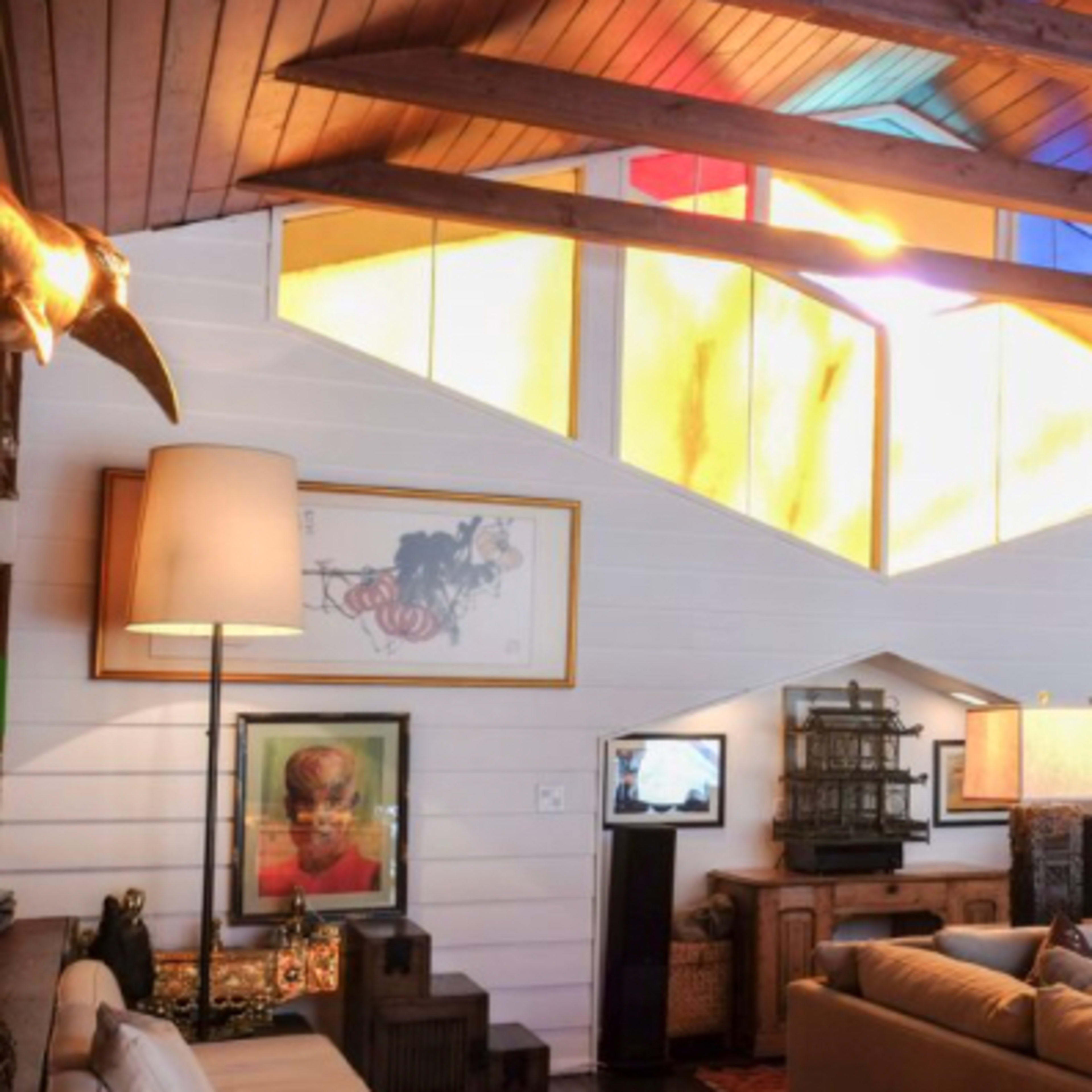 A spacious living room features a high, wooden ceiling with colorful stained glass windows and various art pieces on the walls.