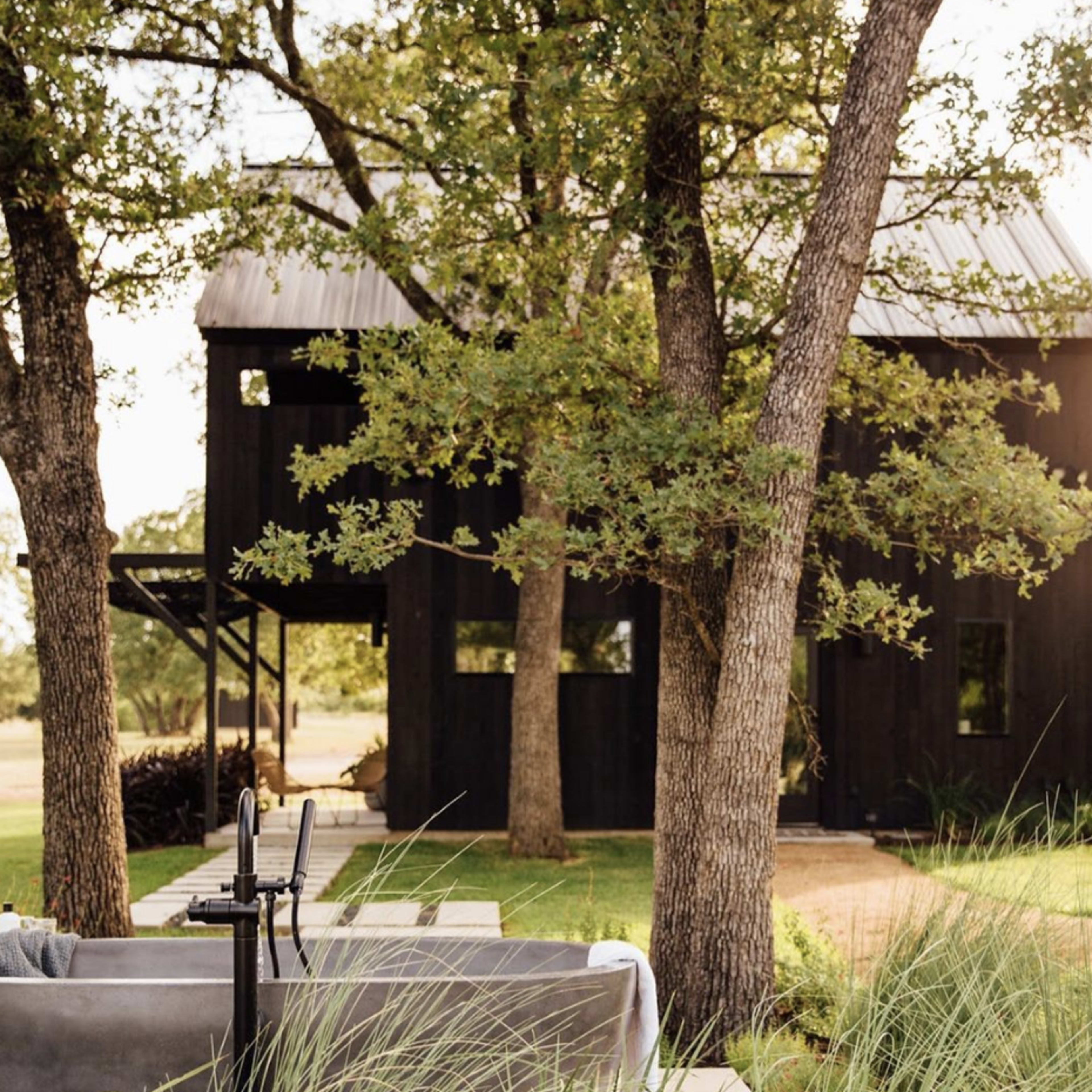 A modern black-clad house is framed by trees, with a patio area visible in the foreground.