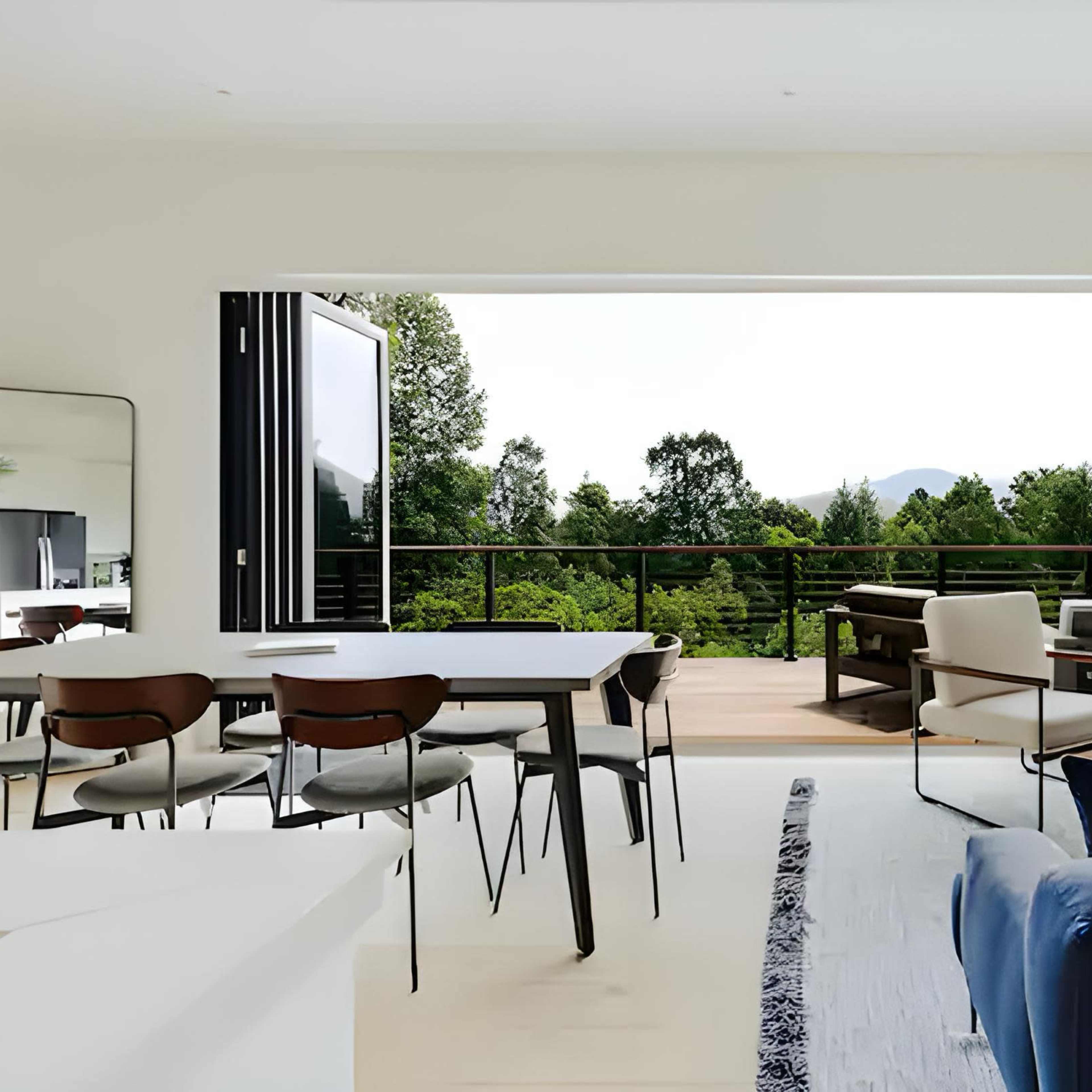 The living area features a large opening to a deck with views of a lush outdoor landscape, furnished with modern seating and a dining table.