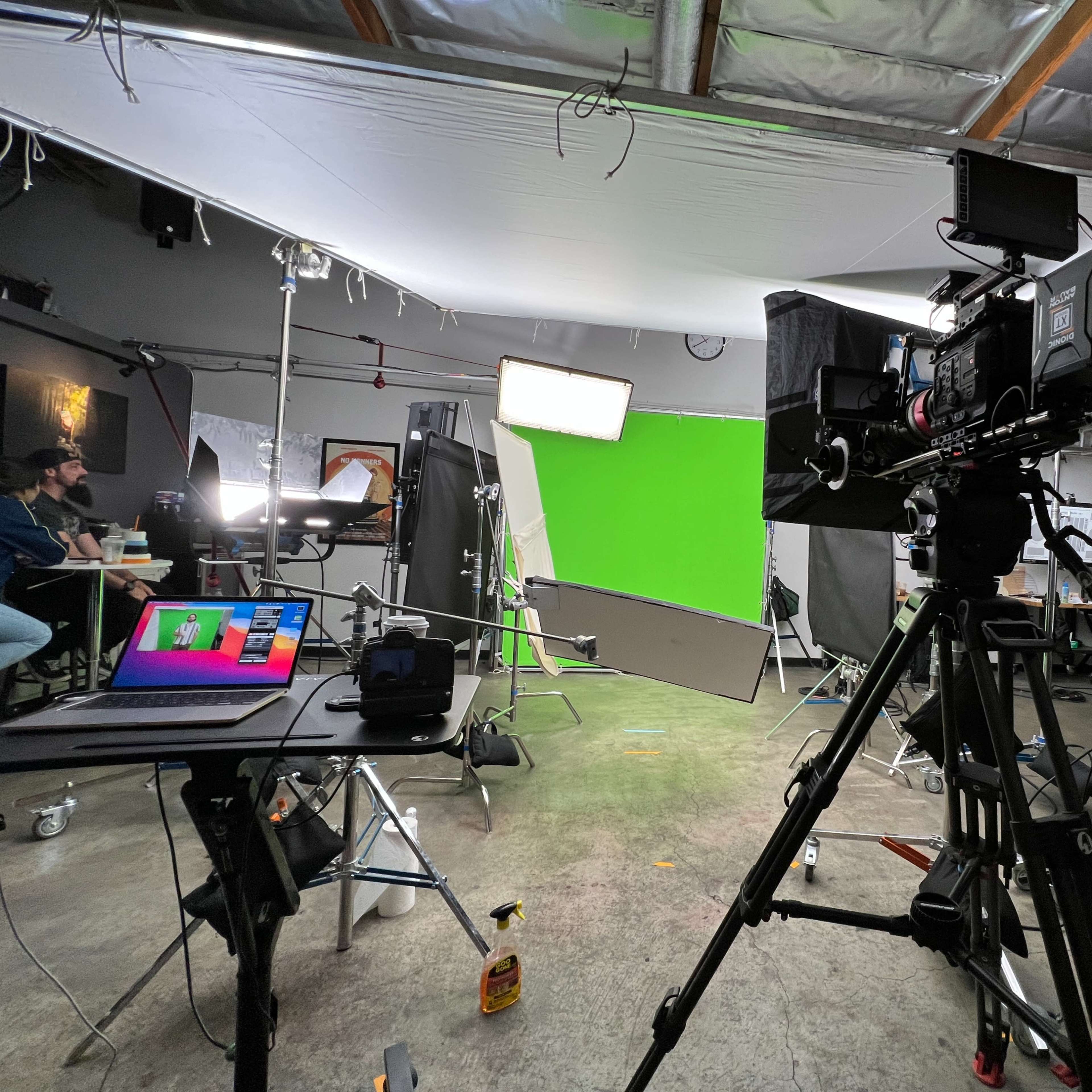 A film set is equipped with a green screen, lighting rigs, and cameras, while crew members prepare in the background.