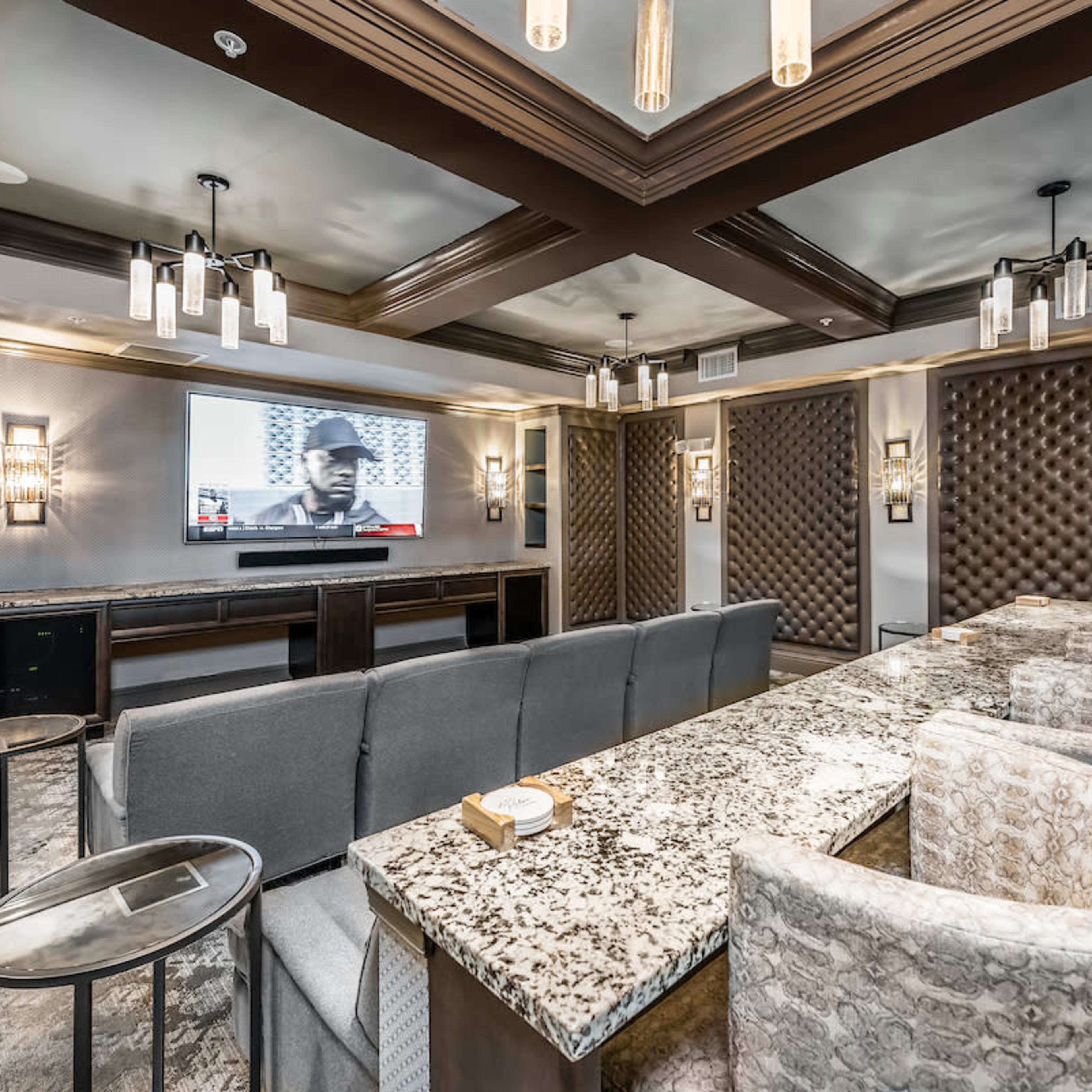 A modern room with a large table, plush seating, and a wall-mounted television featuring a black-and-white image.