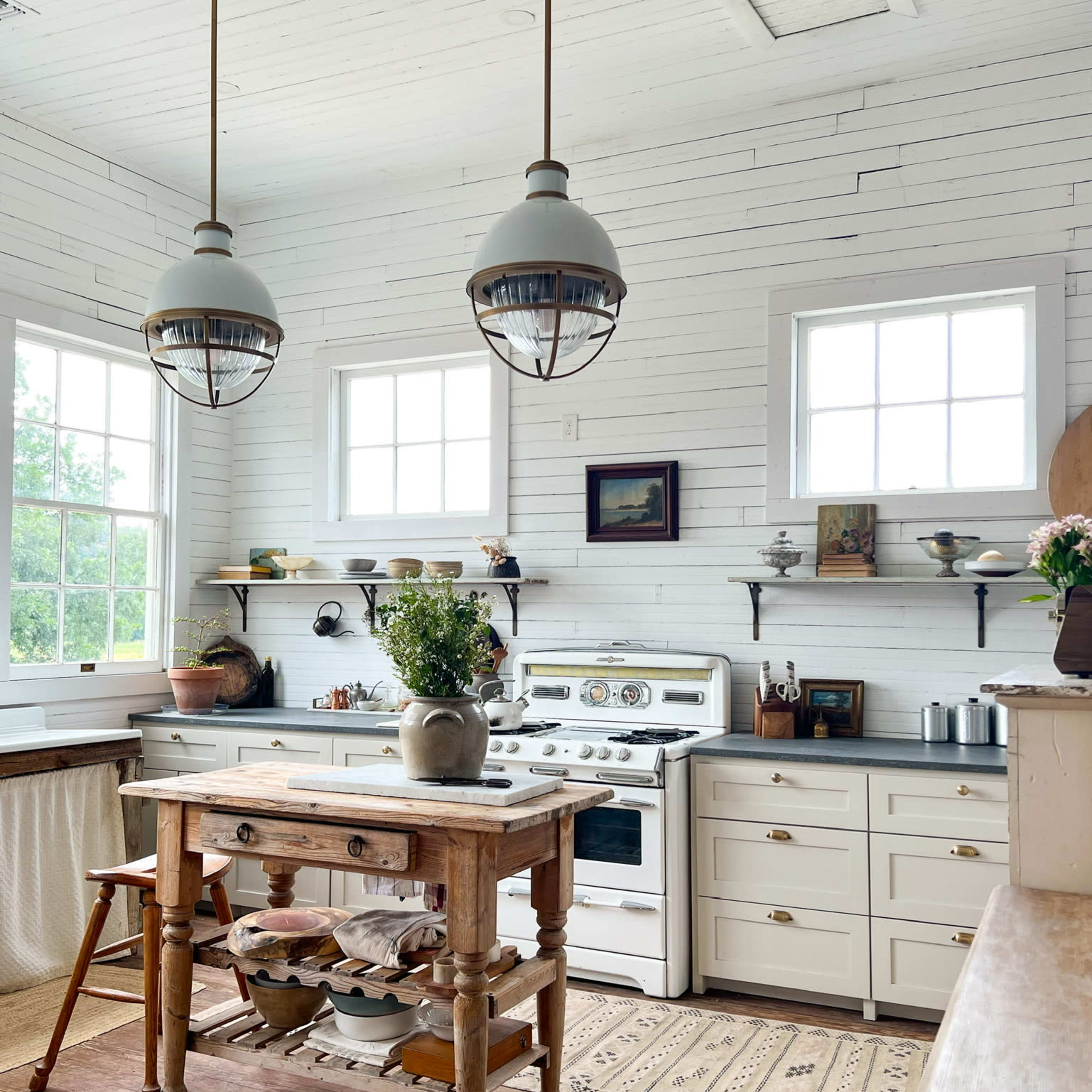 A bright kitchen features white walls, wooden accents, a central table, and large windows.