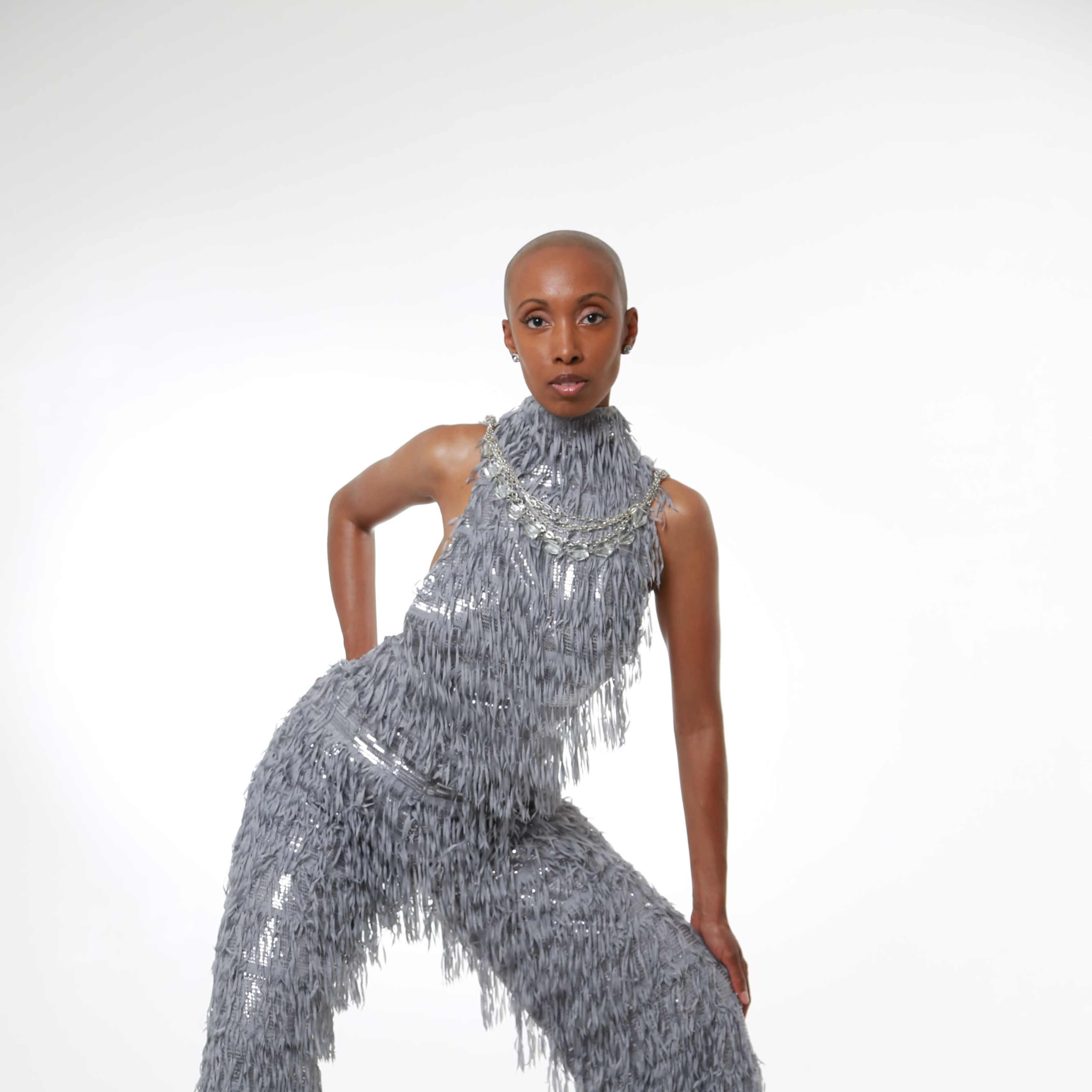 A model poses in a textured gray outfit with fringes against a plain white background.
