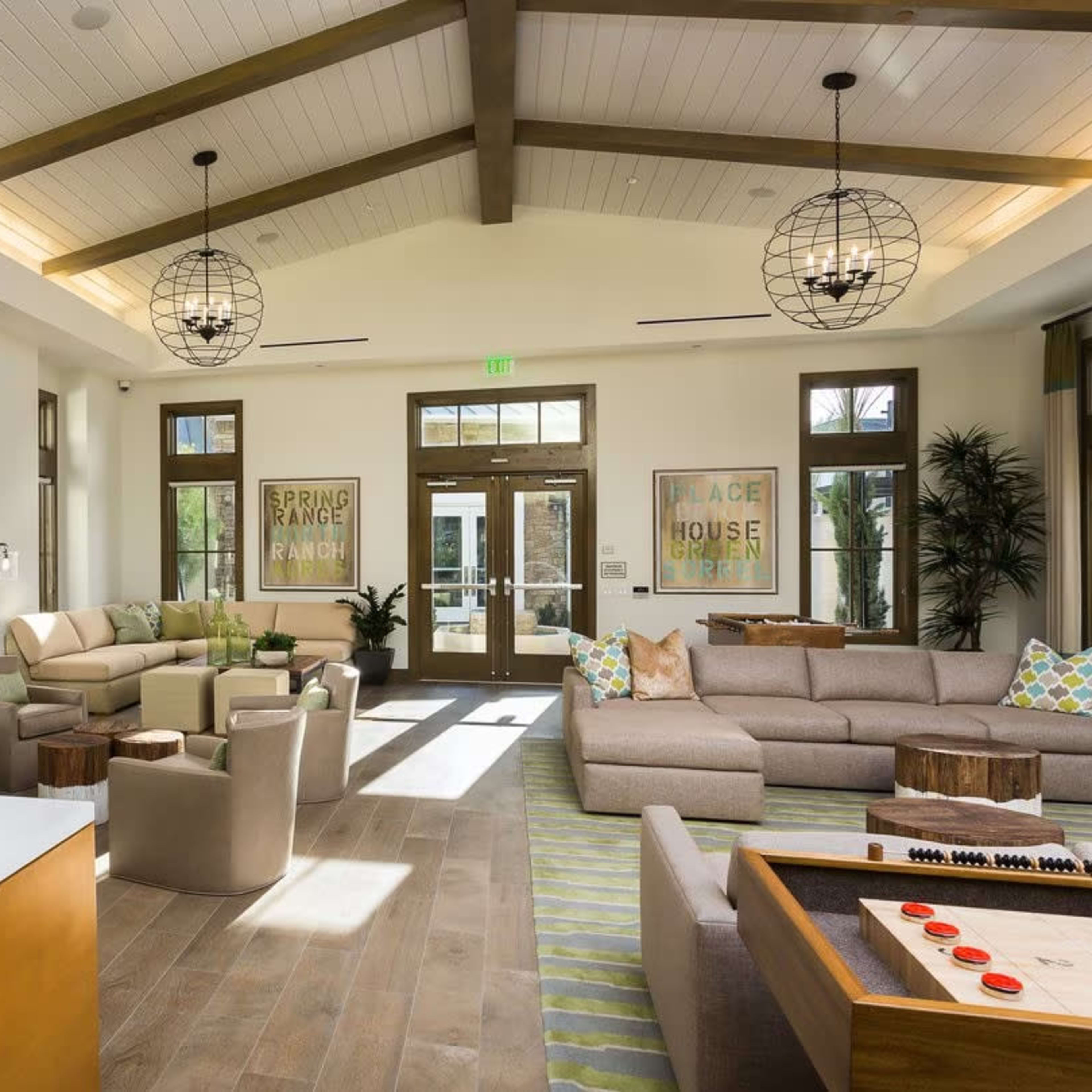 A spacious, well-lit lounge area featuring a modern seating arrangement, large windows, and rustic wooden beams overhead.