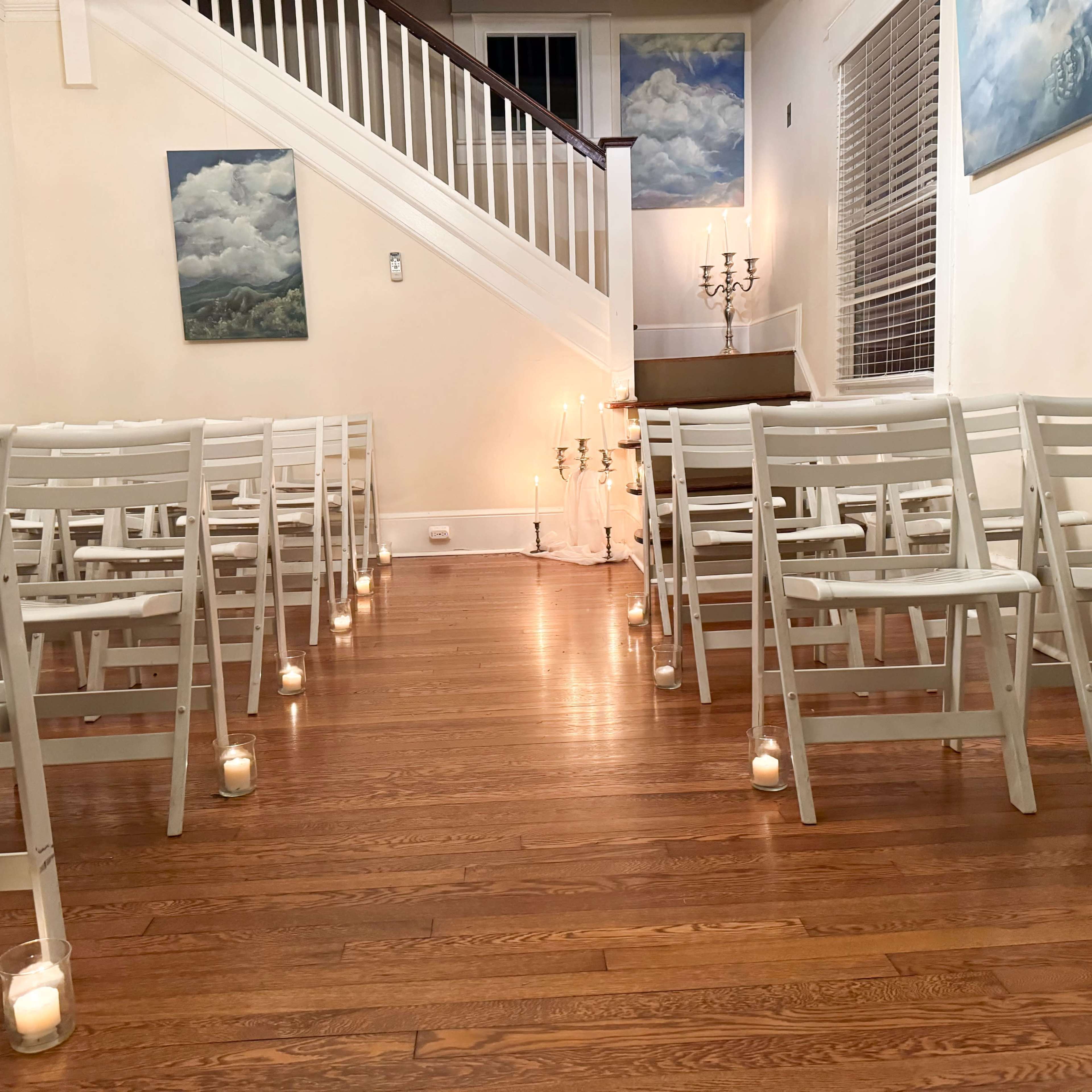A small indoor venue with white folding chairs arranged in rows and candles illuminating the space along a wooden floor.