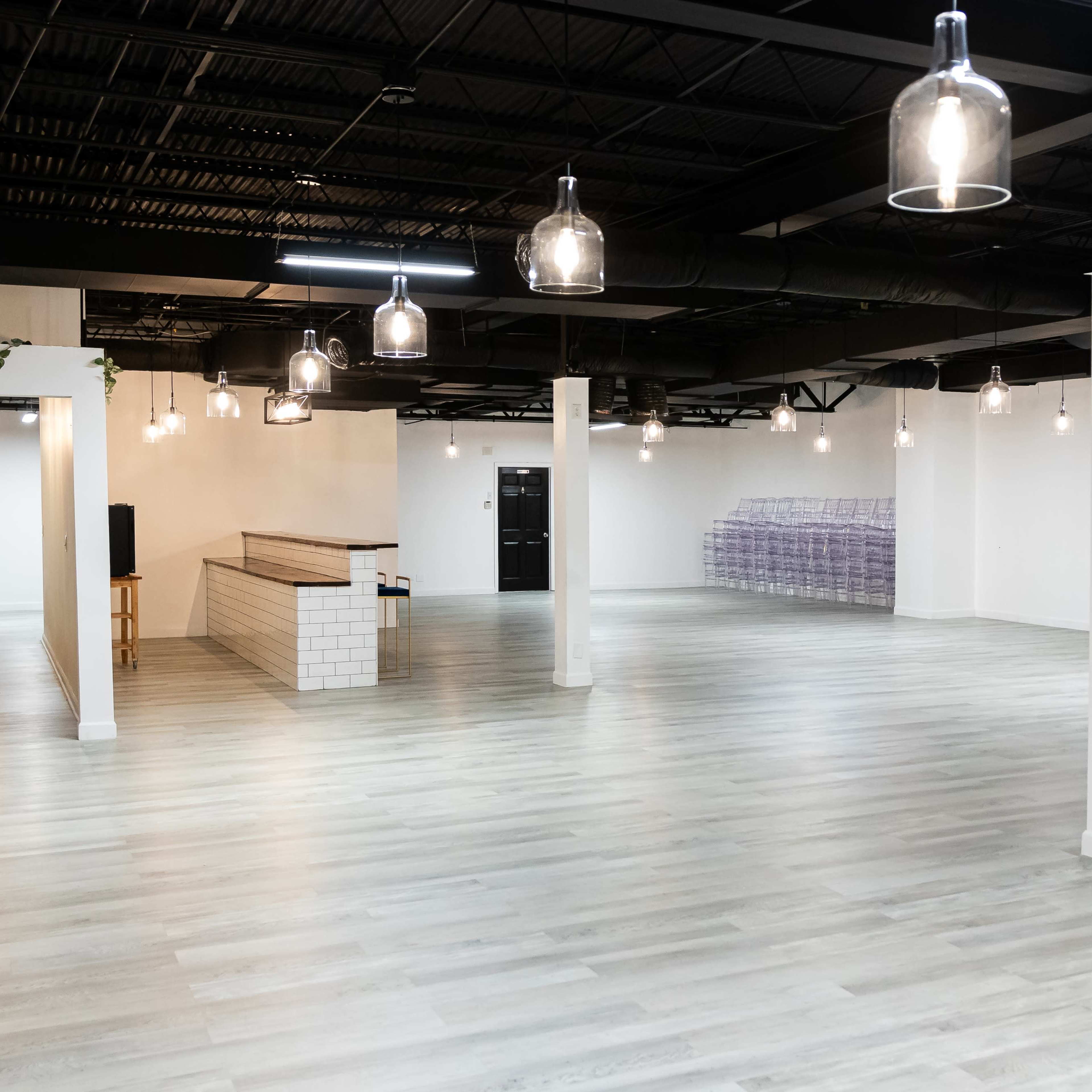 A spacious, empty interior with polished light-colored flooring, white walls, and industrial-style pendant lights hanging from the ceiling.