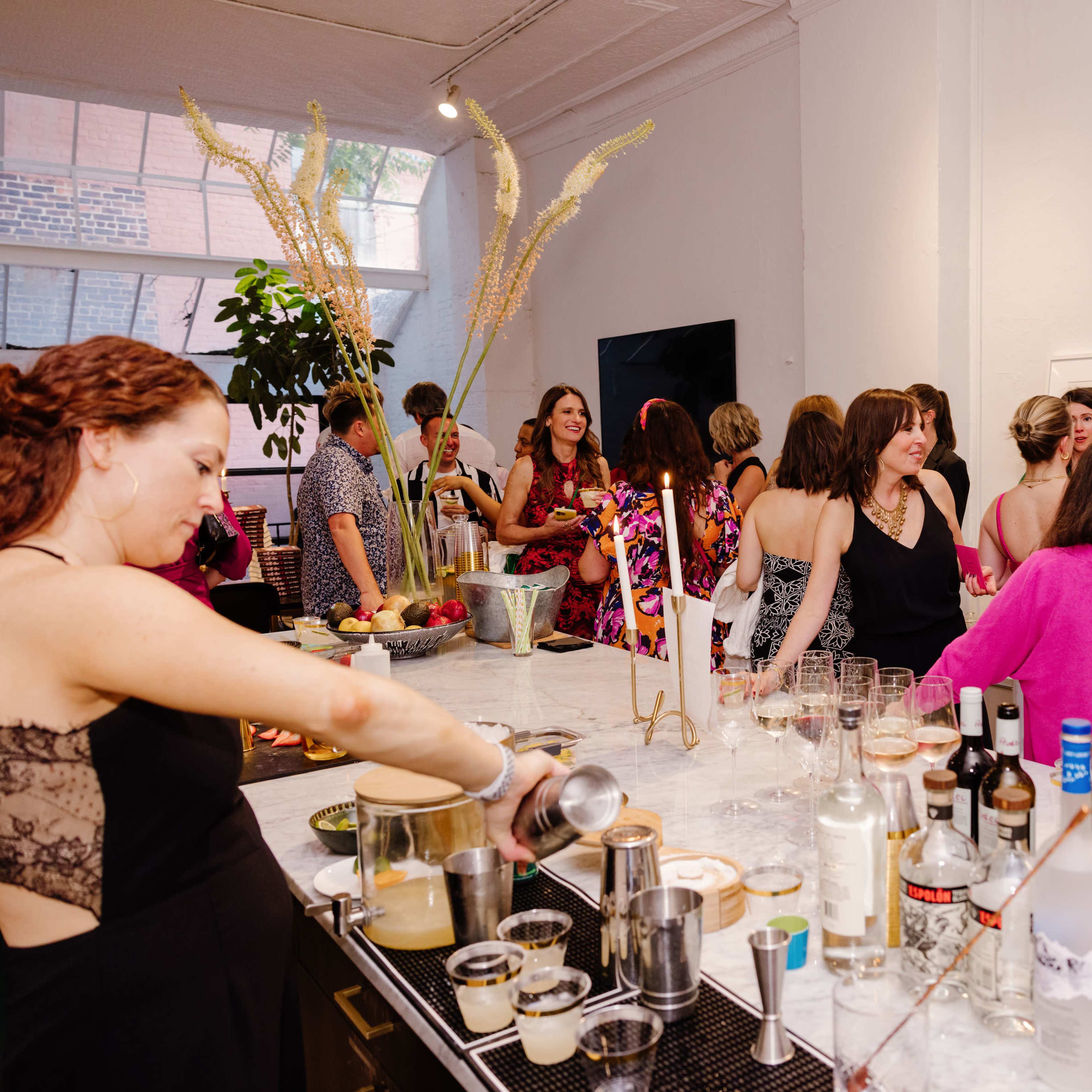 A crowd of people socializes at a lively gathering with a bar area serving various drinks.