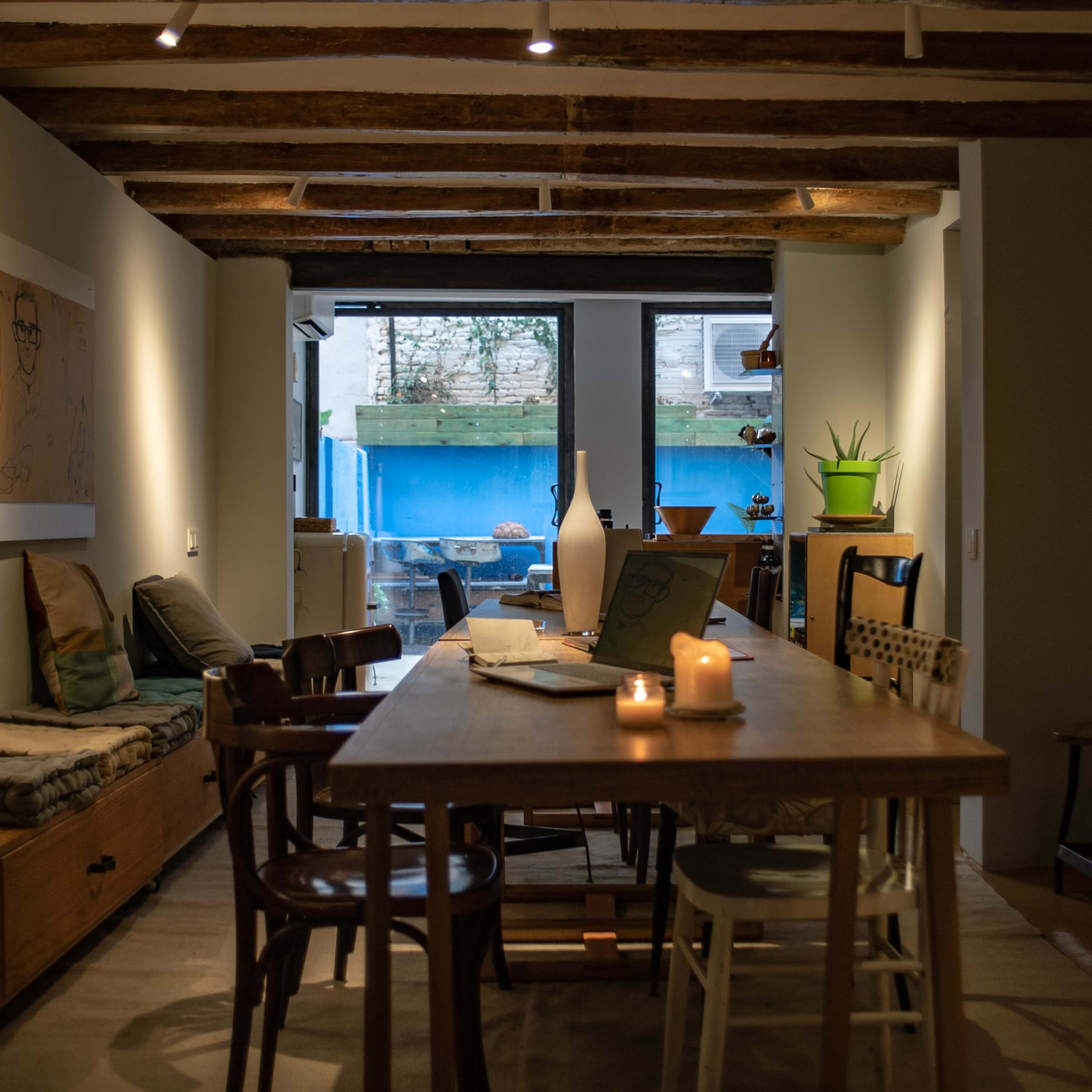 A cozy dining area with a long wooden table, surrounded by various chairs, and a view of a backyard through large glass doors.