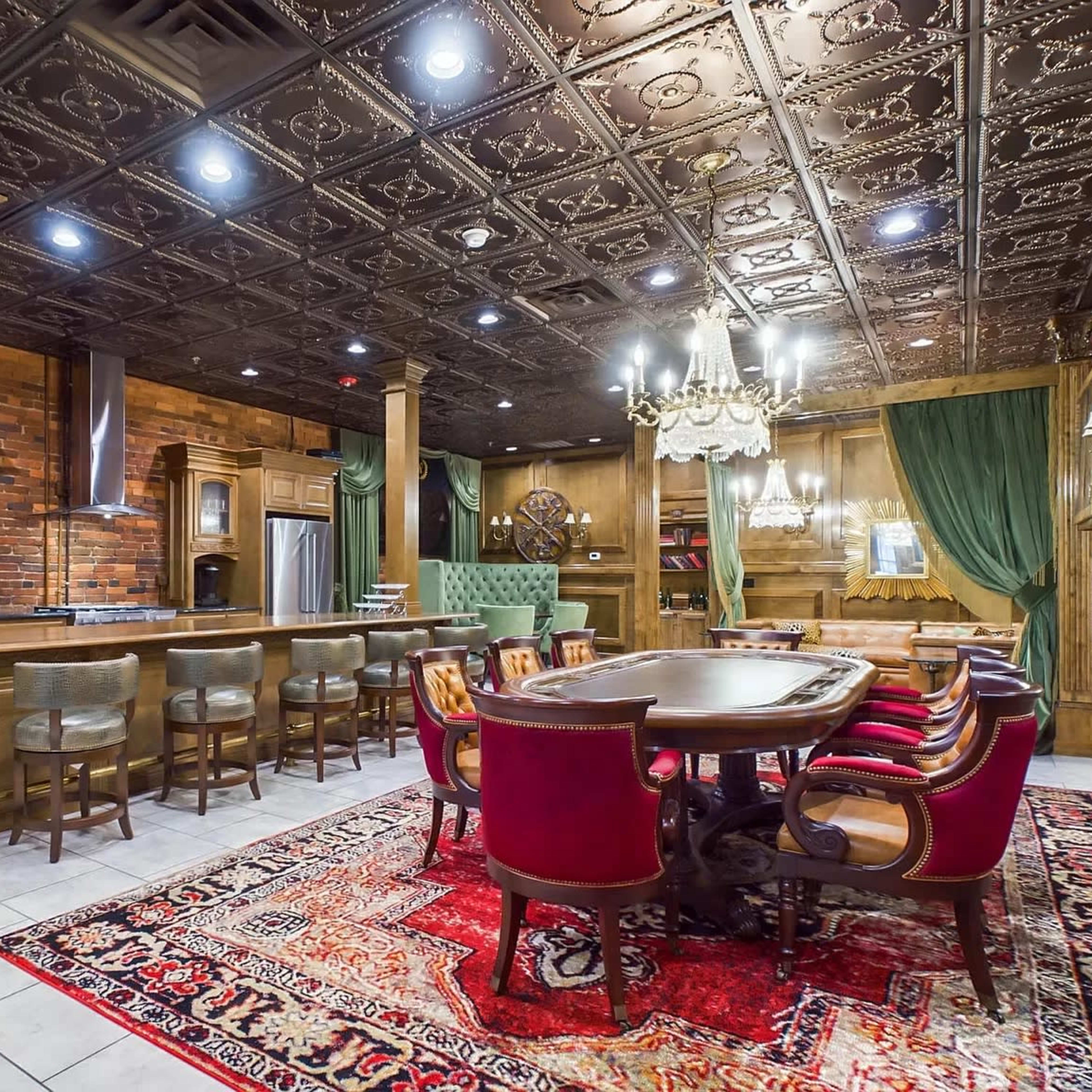 A well-furnished dining area with a large wooden table surrounded by upholstered chairs, a bar counter, and intricate ceiling details in a richly decorated interior.