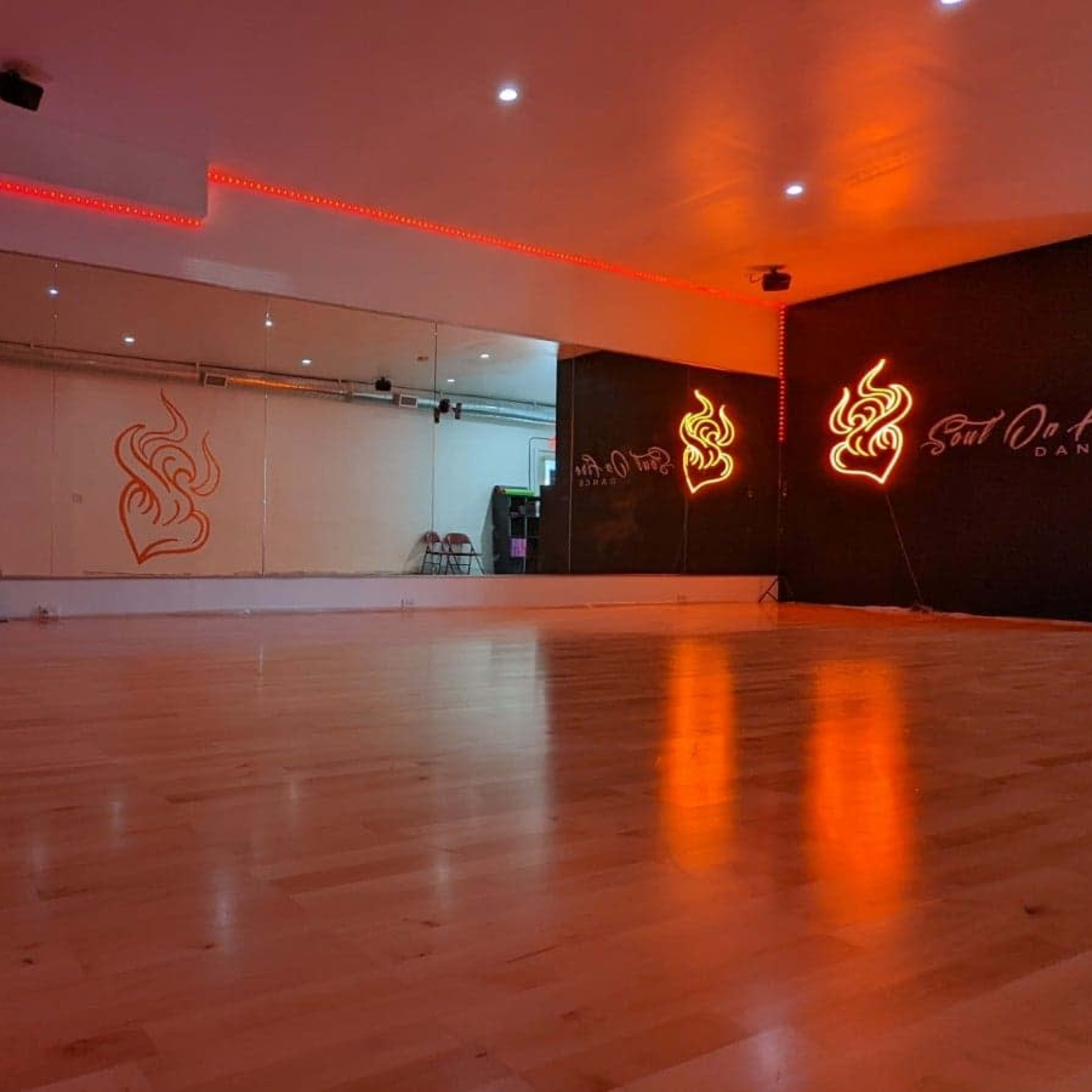 A dance studio with polished wooden floors, mirrored walls, and red lighting accents.