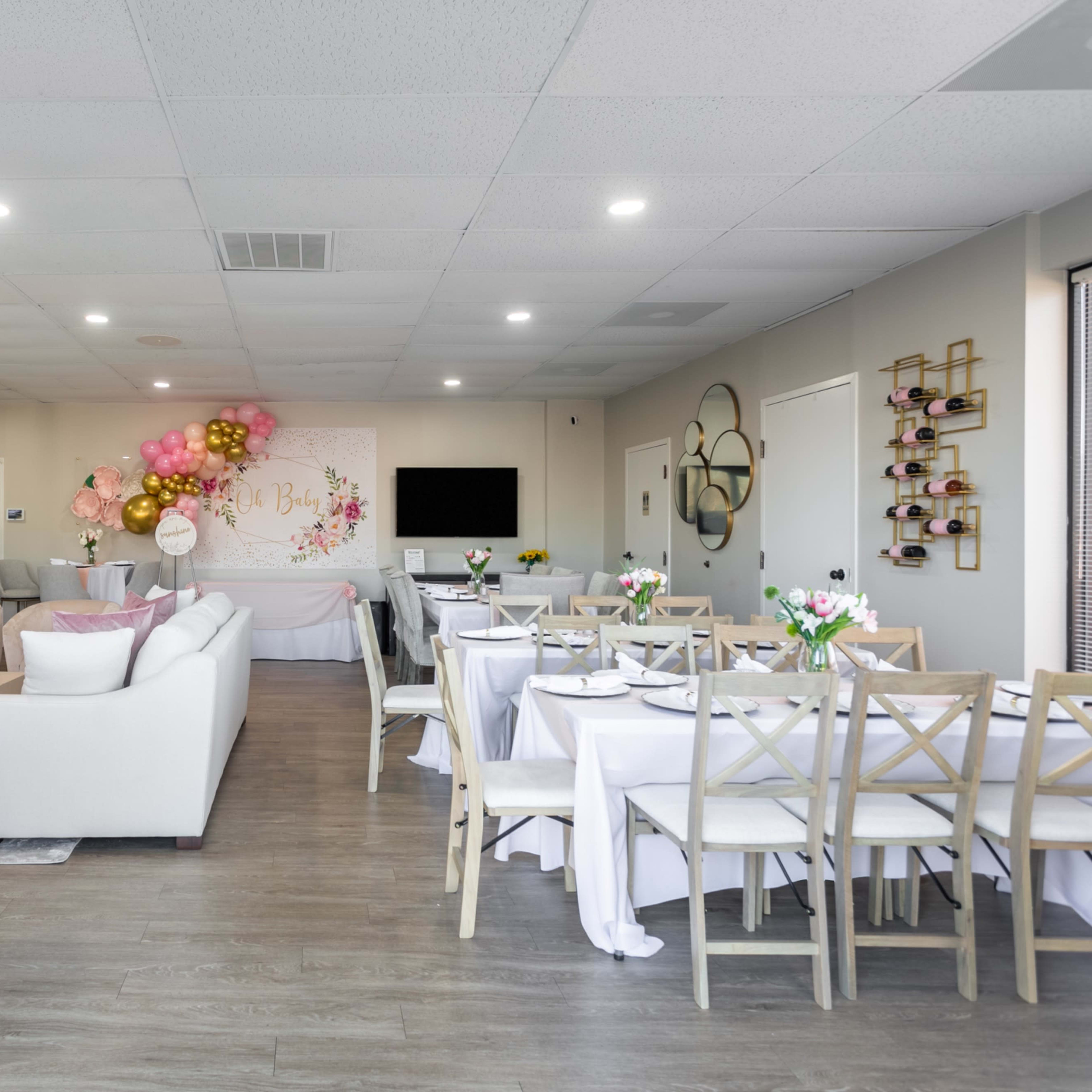 A spacious event room set up with dining tables and chairs, decorated with balloons and floral centerpieces.