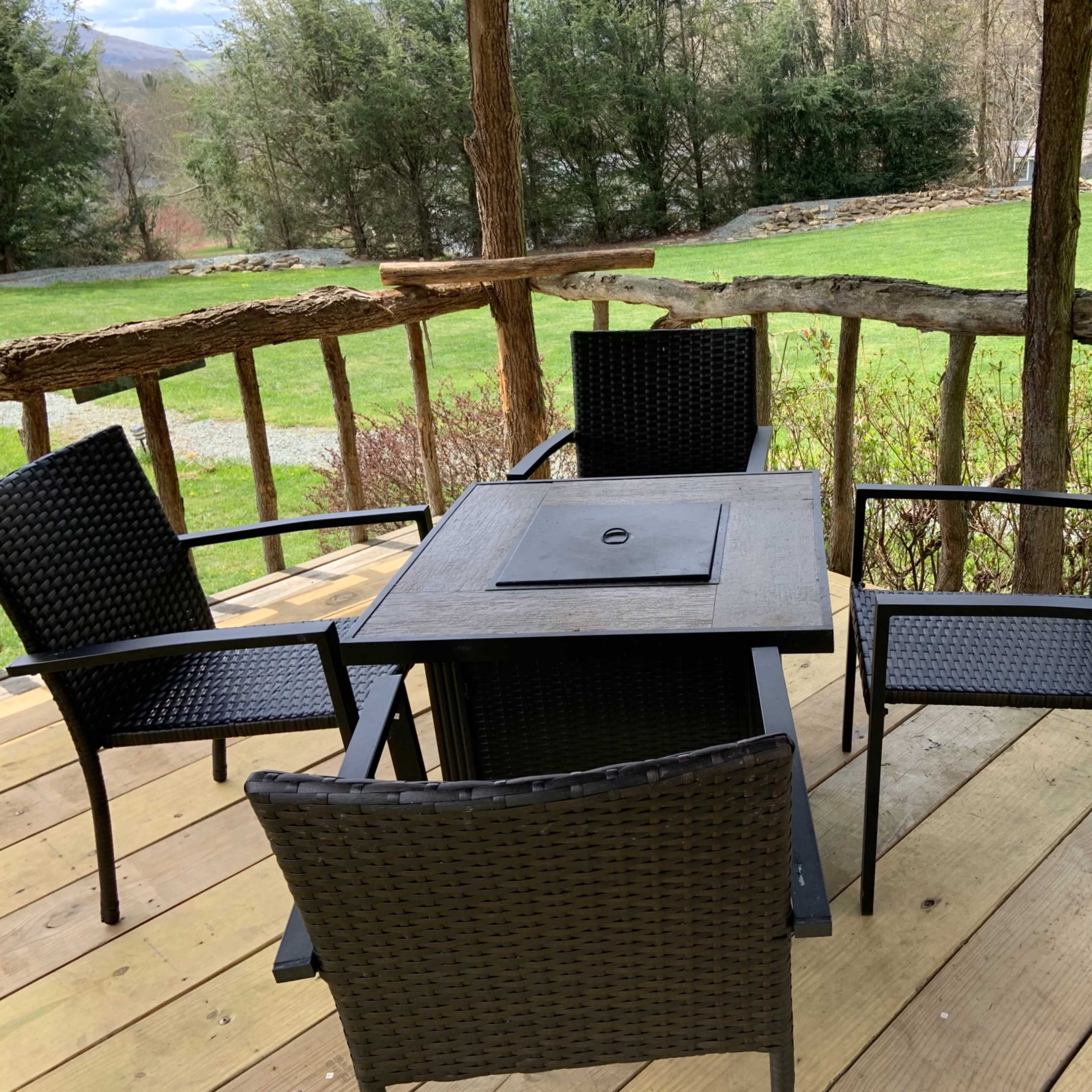 A patio with a rectangular table and four chairs surrounded by wooden railings and a view of a grassy lawn and trees.