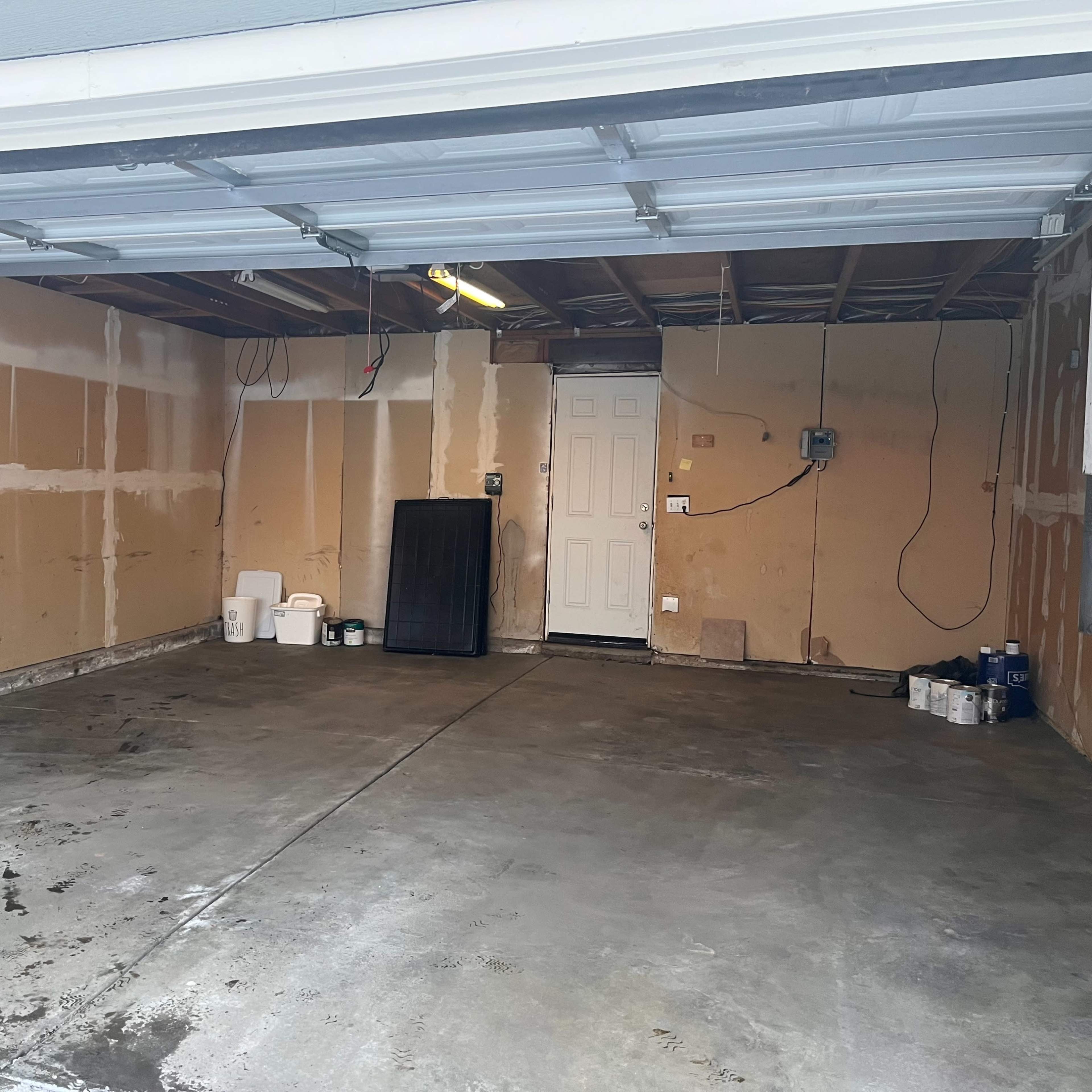 An empty garage with a concrete floor and beige drywall partially exposed on the walls.