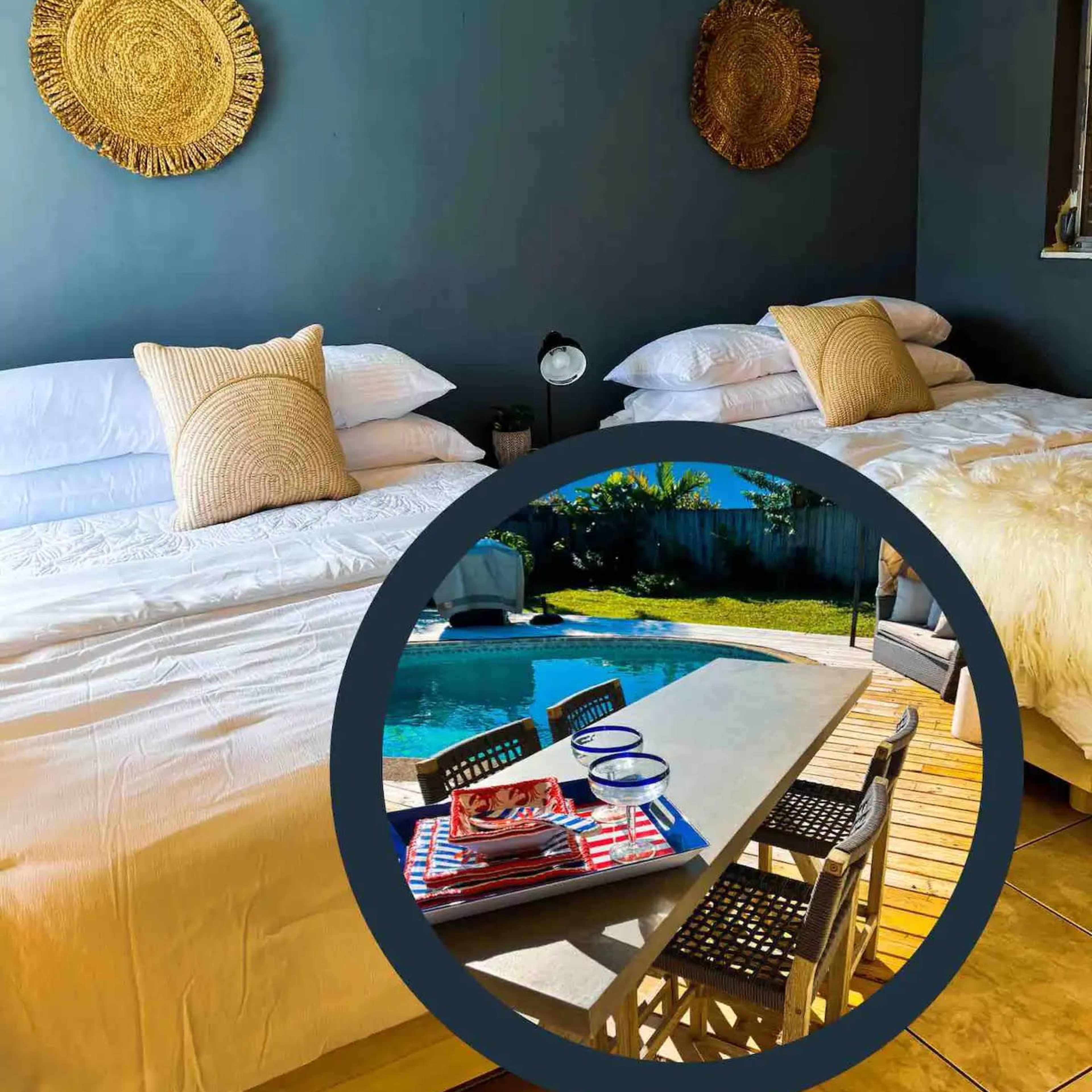 A well-lit room with two beds, a decorative wall, and a small dining table set up outdoors near a pool.