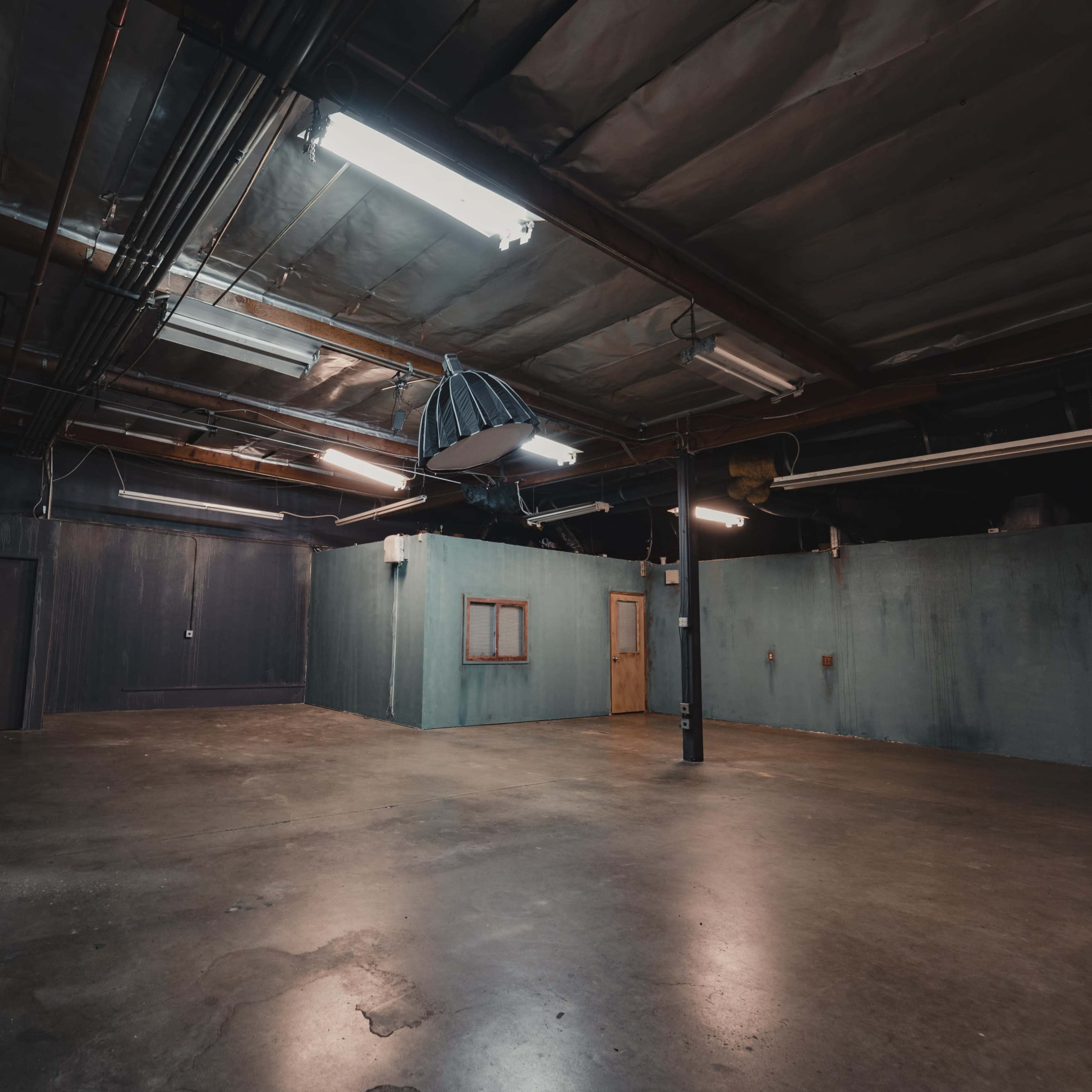 An empty industrial room with bare concrete flooring, dim lighting, and walls painted in dark colors.