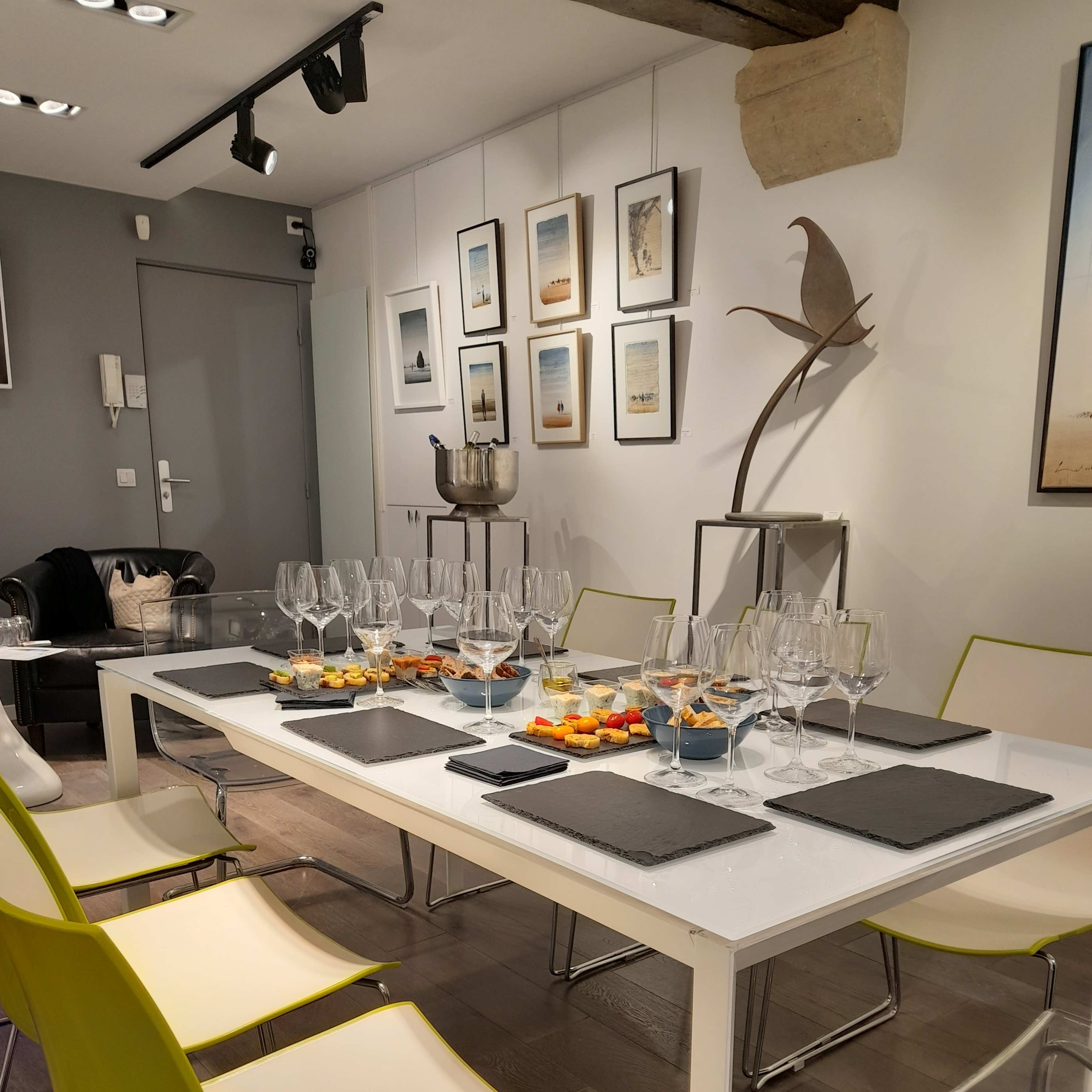 A dining table set with glasses and snacks is surrounded by modern chairs in a well-lit room adorned with framed images on the walls.