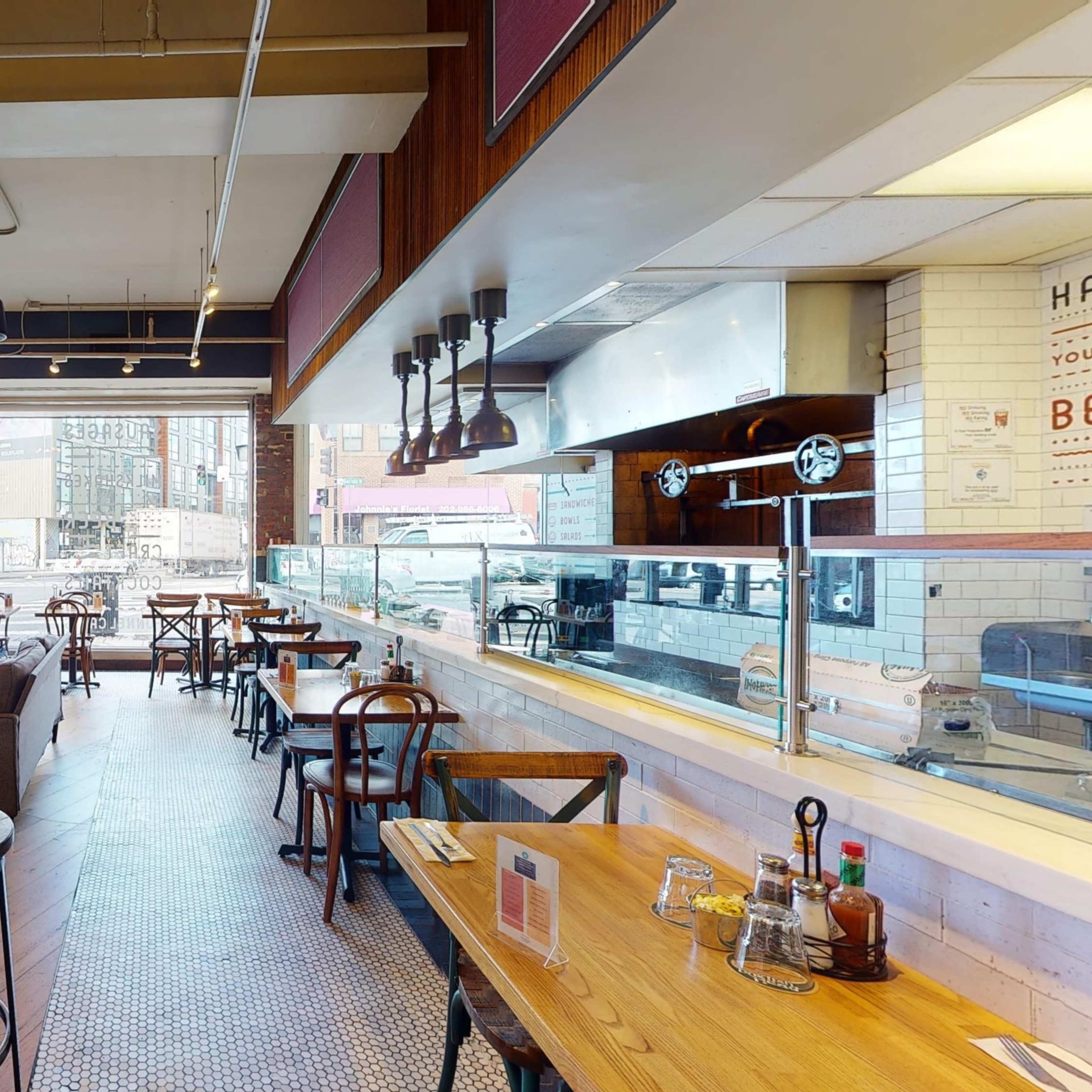 A spacious café with wooden tables and chairs, exposed brick walls, and a glass display counter.