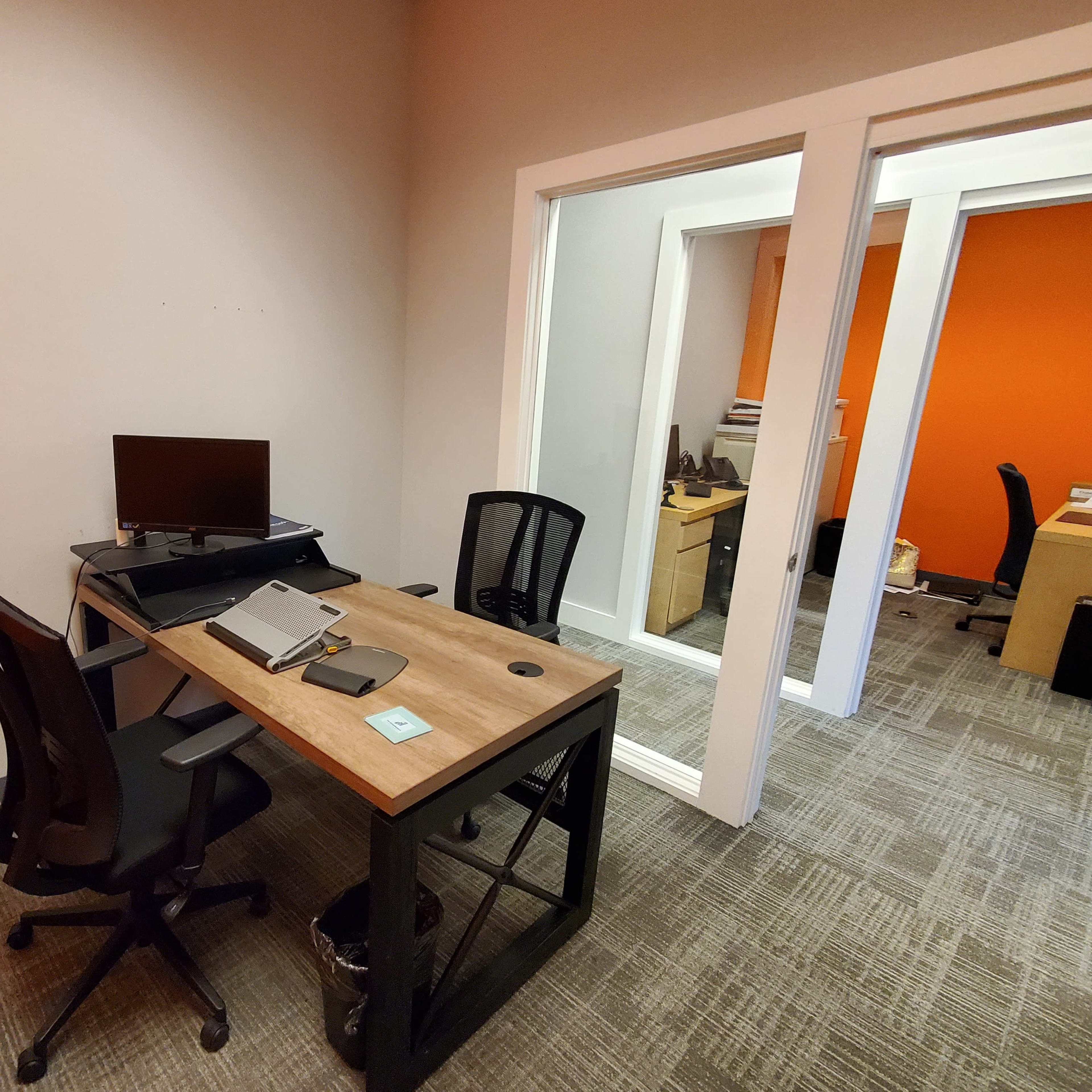 A small office space featuring a desk with a monitor and a chair, set against an orange wall.