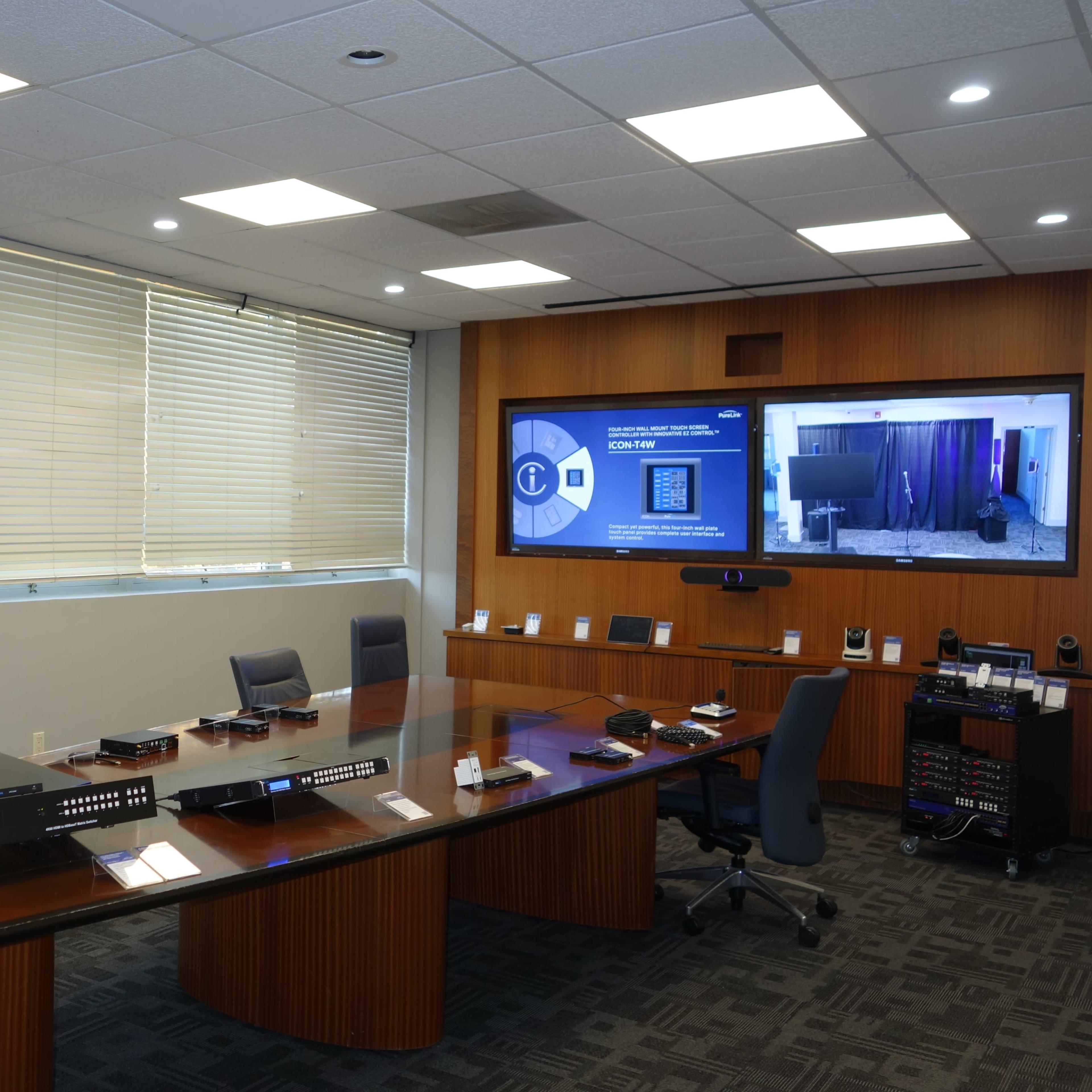 A modern conference room equipped with a large table, multiple screens, and a variety of audio-visual equipment.