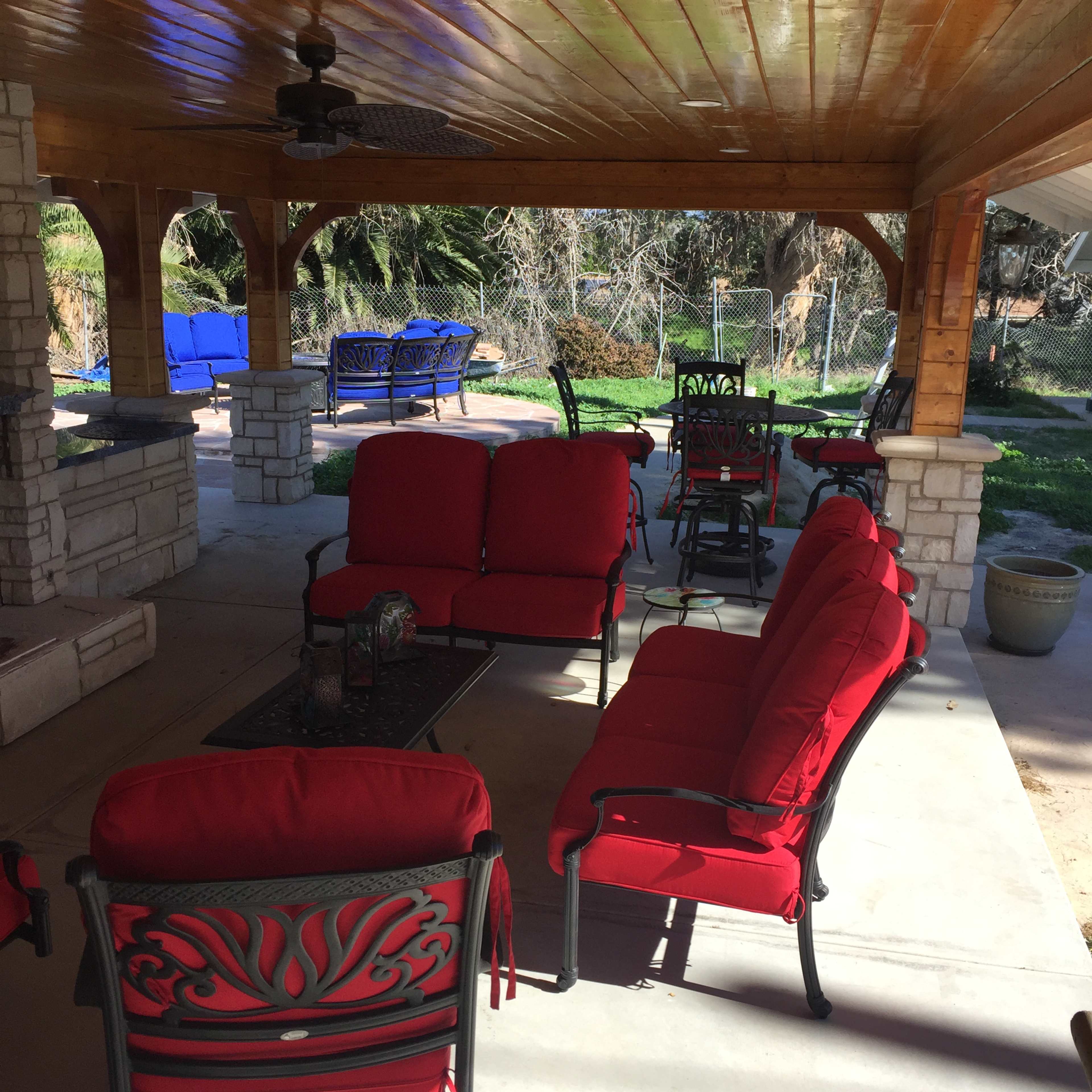 A covered outdoor seating area with red cushioned furniture arranged around a low table.